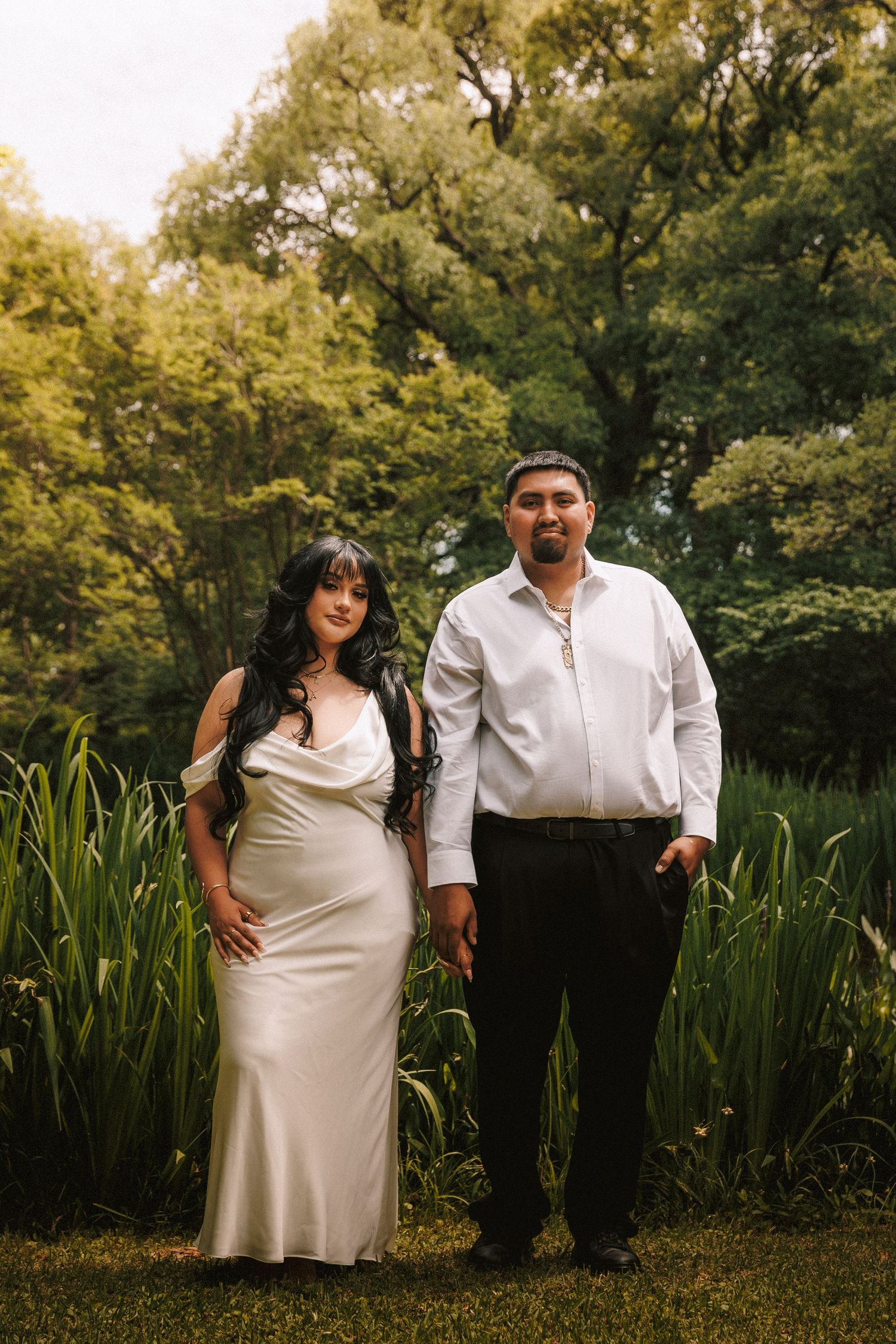 A romantic maternity photo series shows an expecting couple in white outfits playfully posing together in a garden setting.