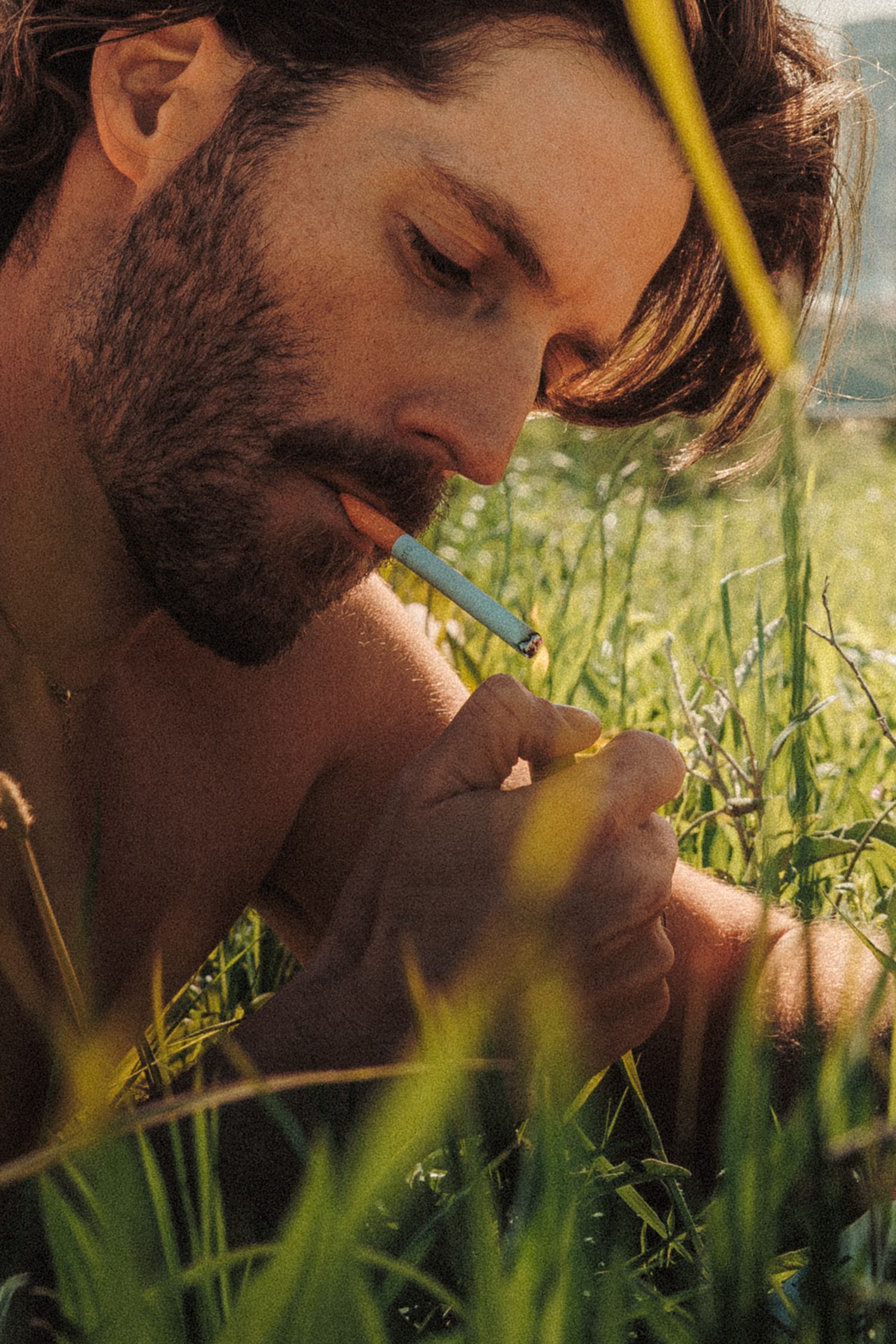 Close-up profile view of someone smoking while lying in tall grass on a sunny day.