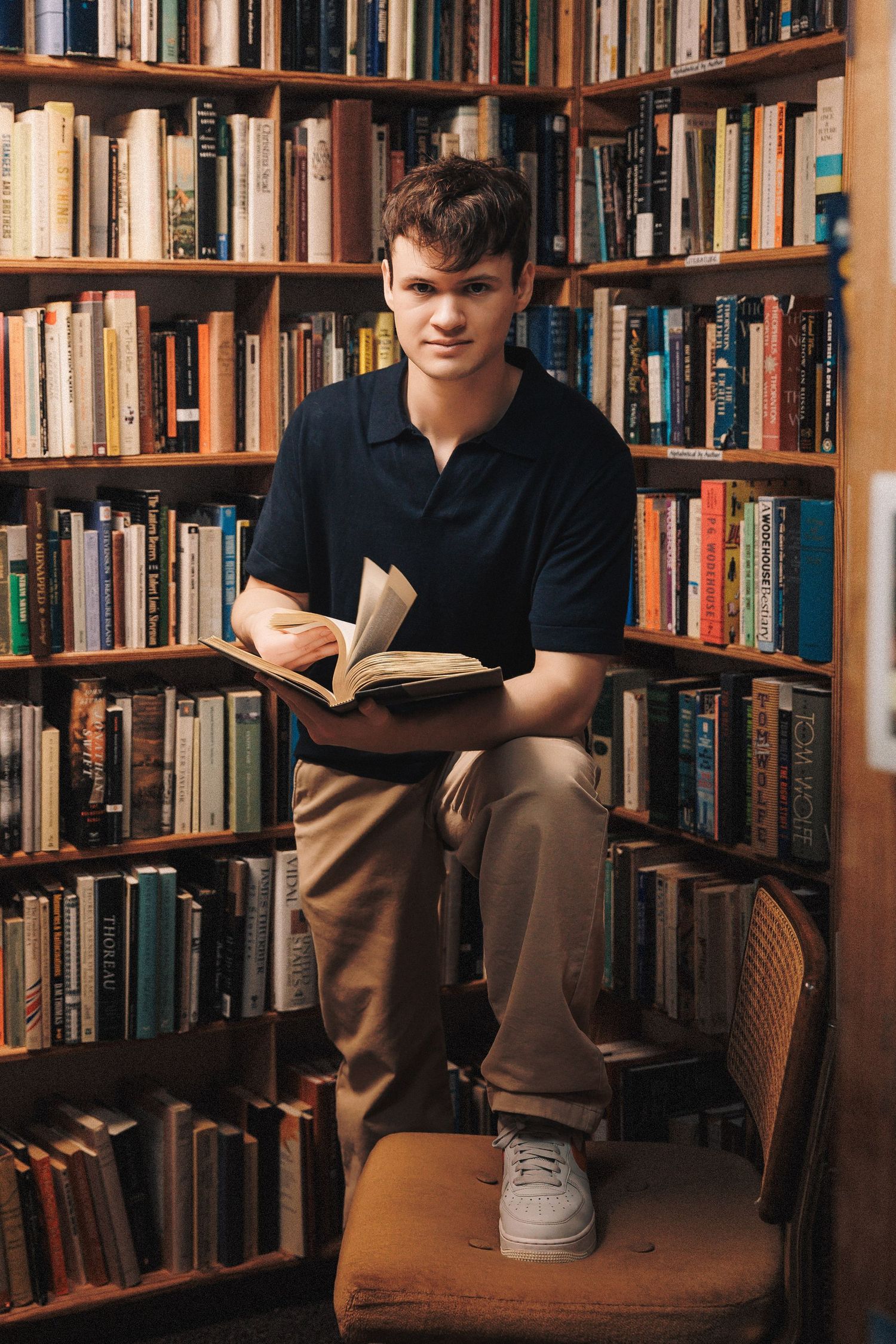 Someone reads a book while sitting comfortably in a cozy library corner surrounded by wooden bookshelves filled with volumes.