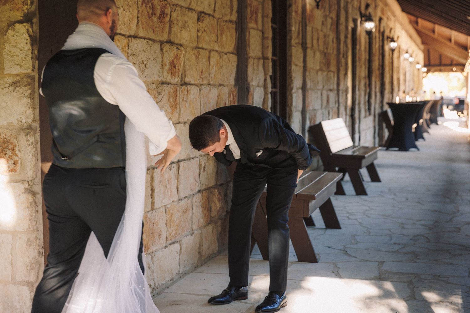 Emotional groom bowing his head during first look moment with bride in white gown at stone wedding venue.