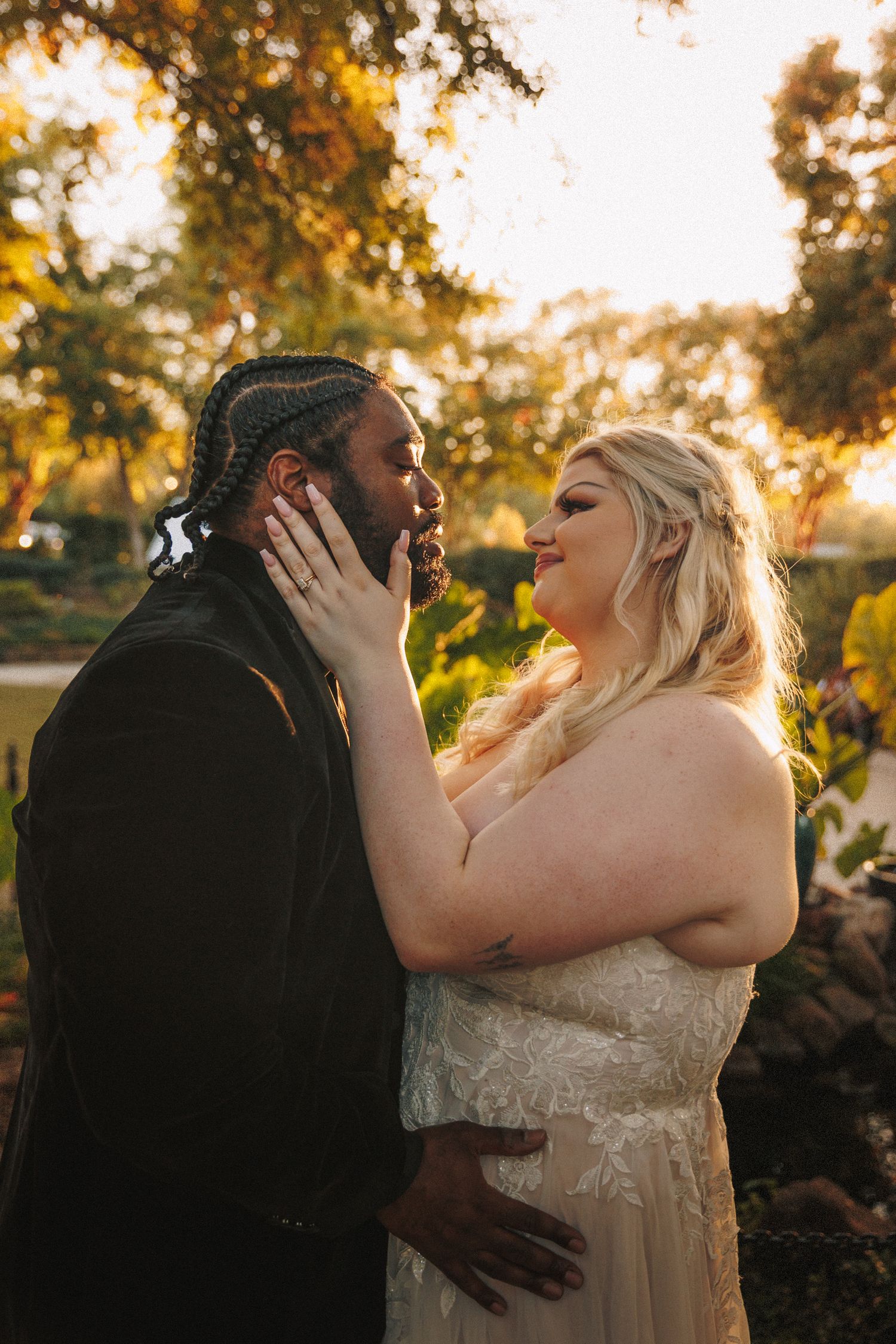 Interracial couple sharing a romantic moment in golden sunset light at their wedding.