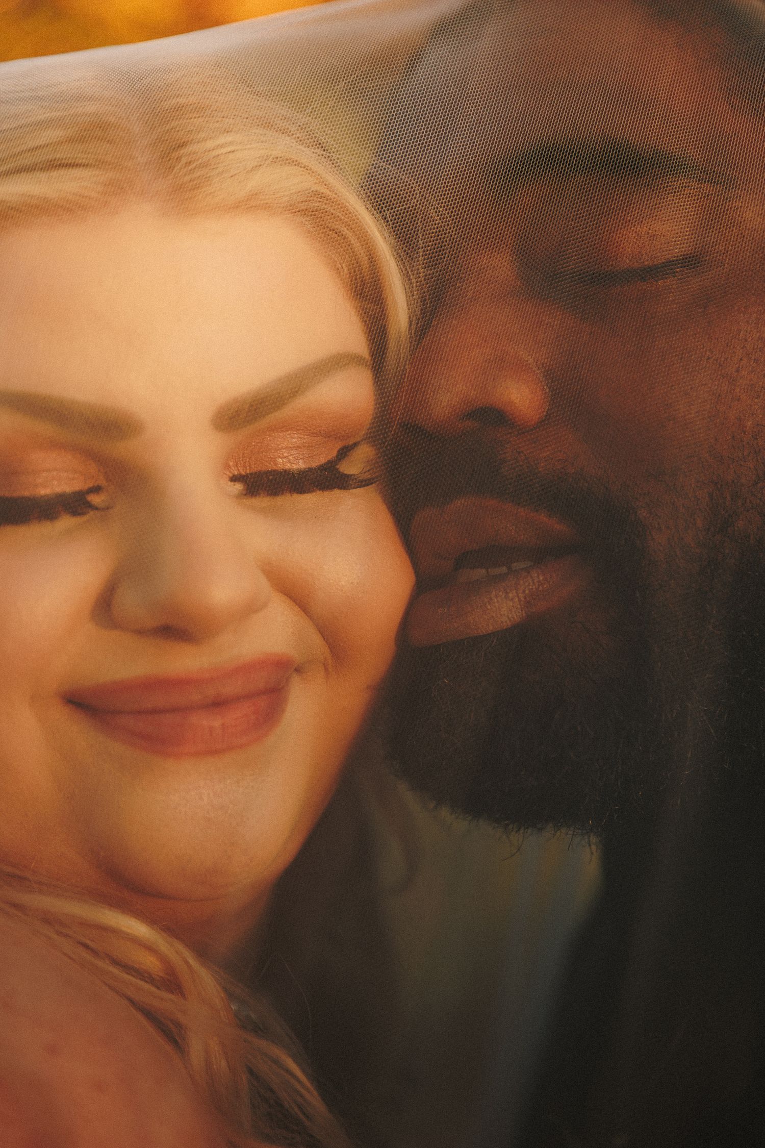 Close-up of interracial newlywed couple sharing intimate moment under bridal veil.