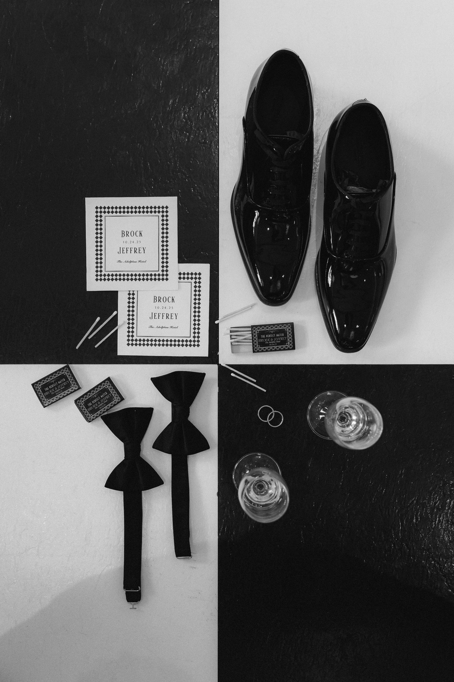 Black and white flat lay of groom wedding accessories including patent leather shoes, bow ties, rings, and invitations.