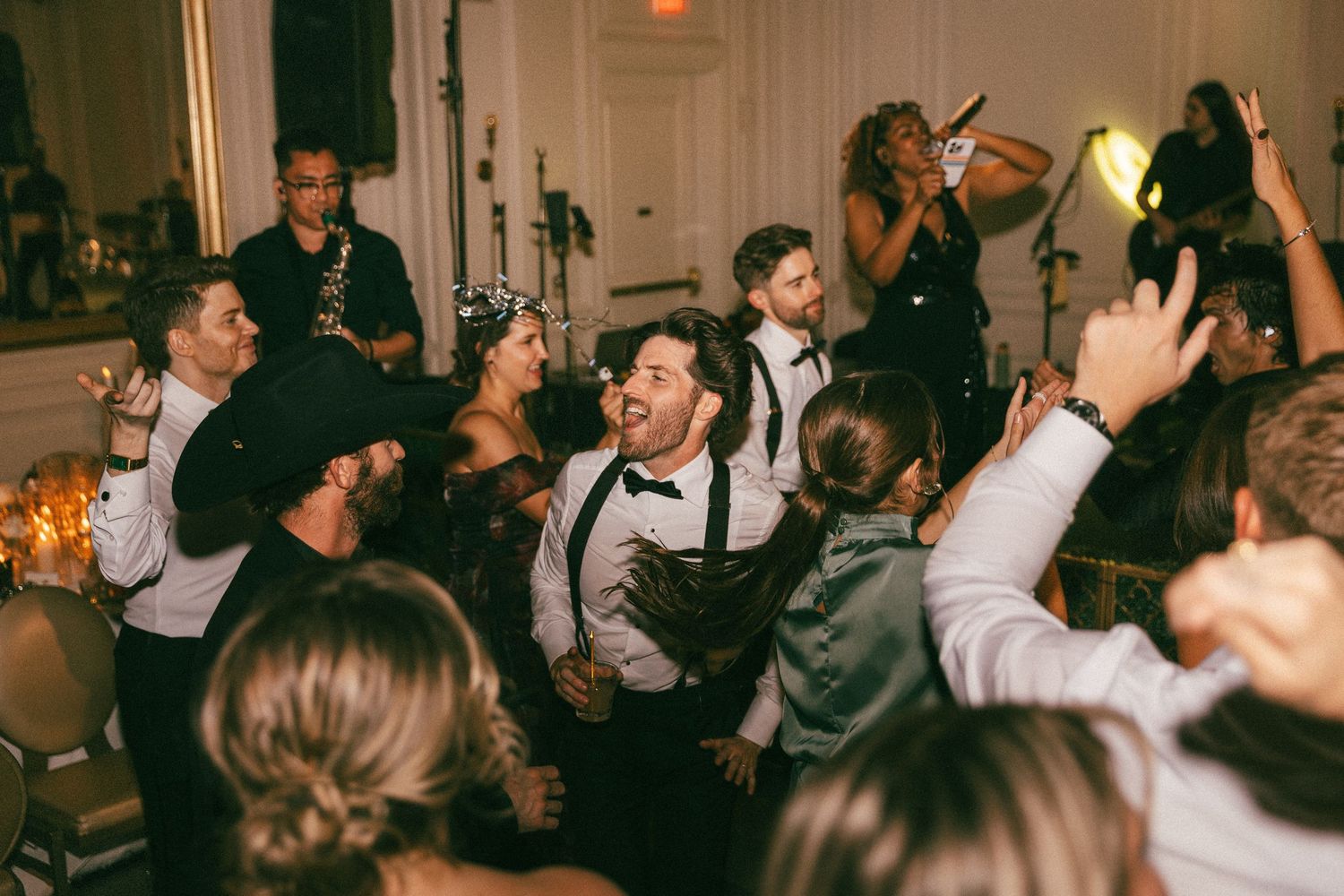 Lively wedding reception dance floor with guests and groom celebrating joyfully with live band.