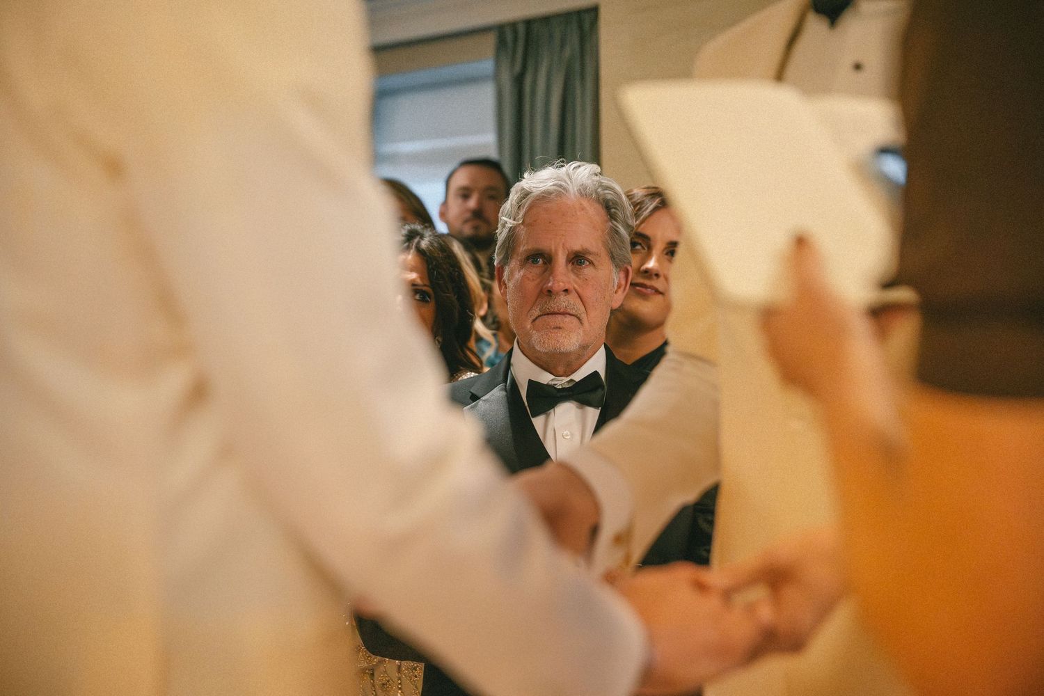 Emotional wedding guest in black bow tie watching couple exchange vows at ceremony.