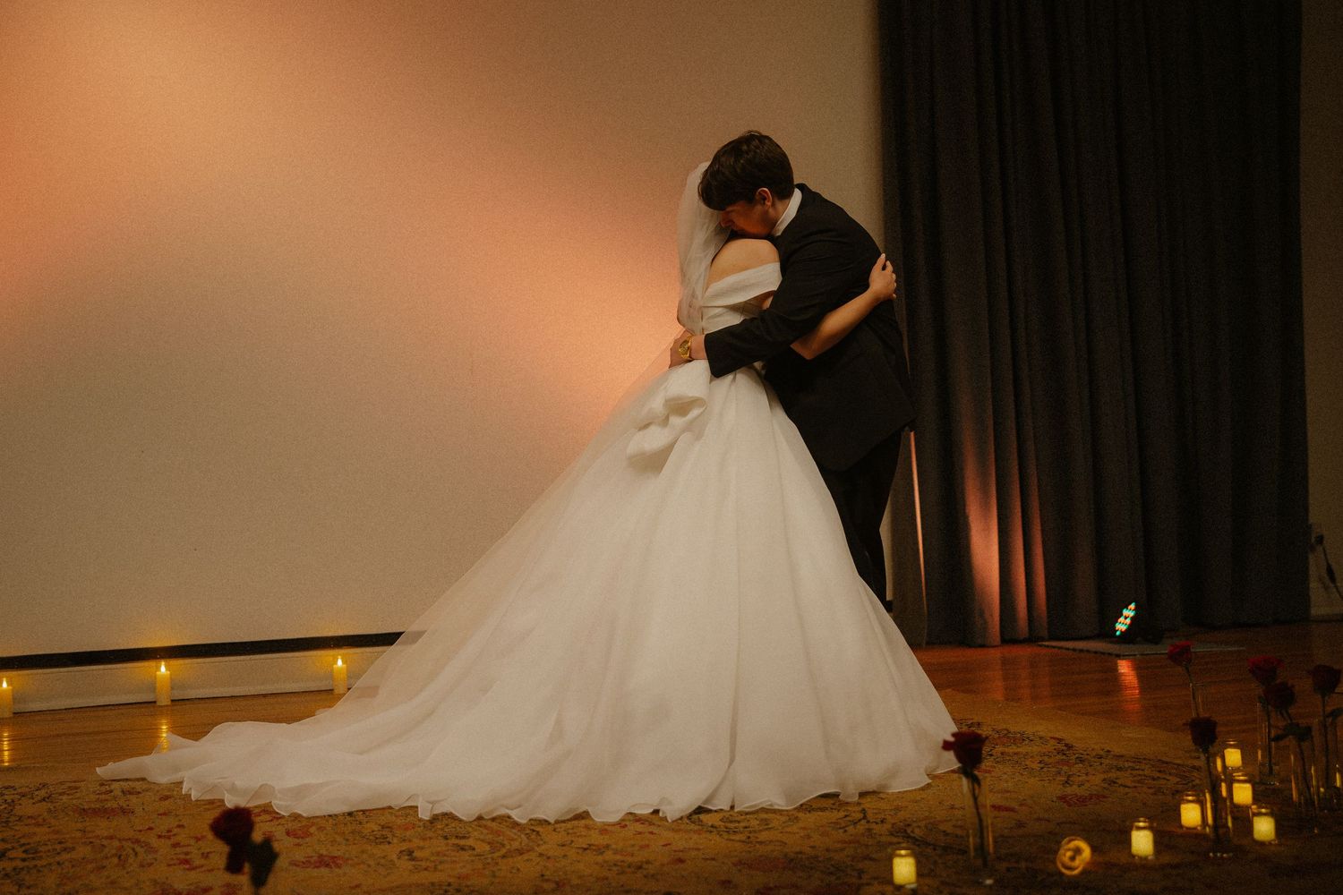 Bride and groom share first dance embrace in white ballgown with candles on wedding day.