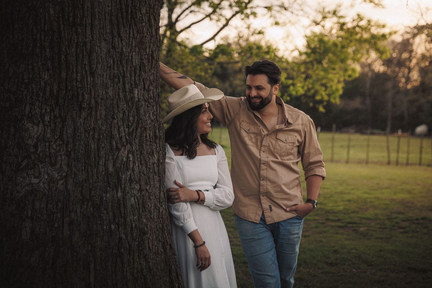 Couple sharing a sweet moment by a large tree at golden hour in a lush green park.