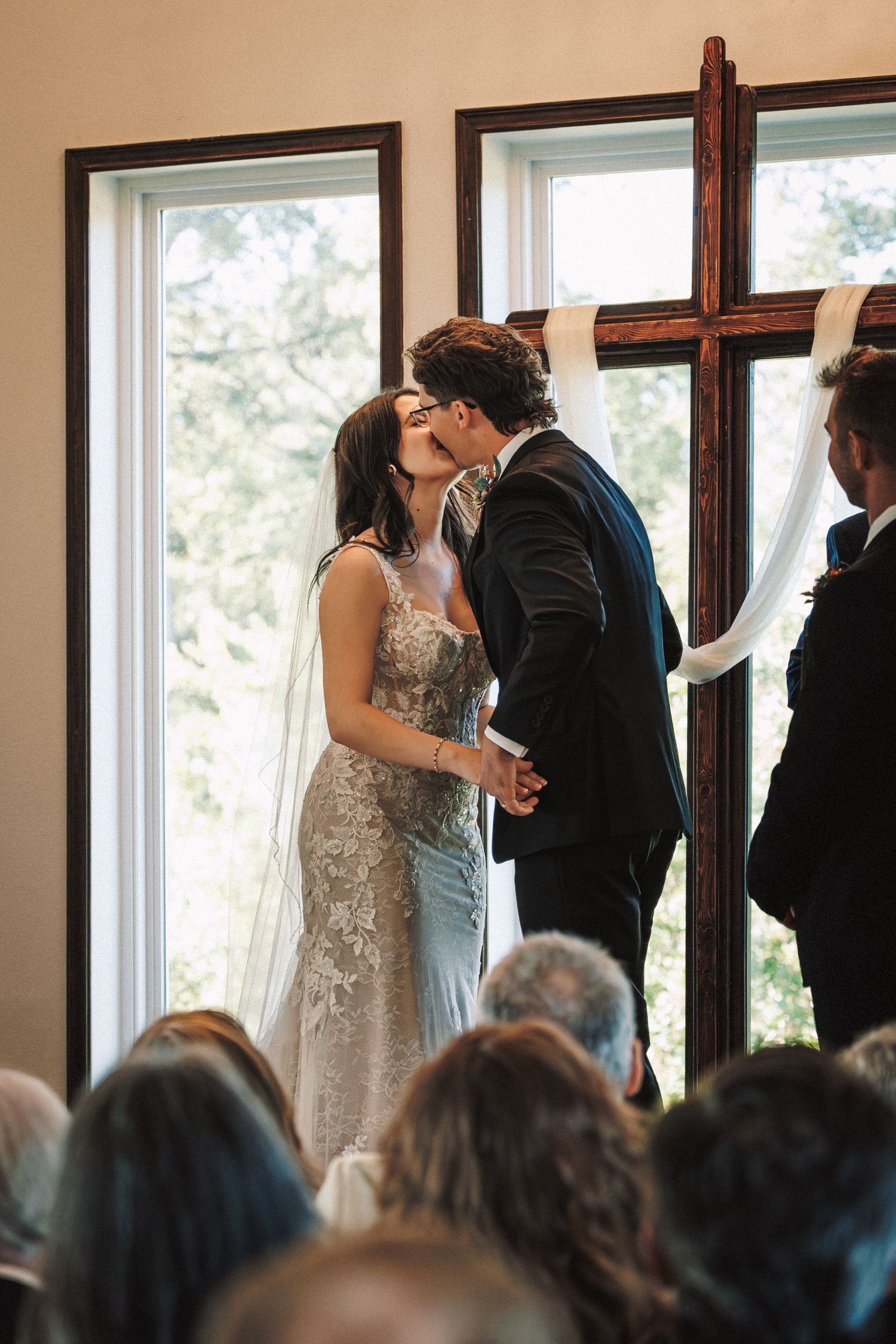 Bride and groom sharing their first kiss at the altar beneath a wooden cross during their ceremony.
