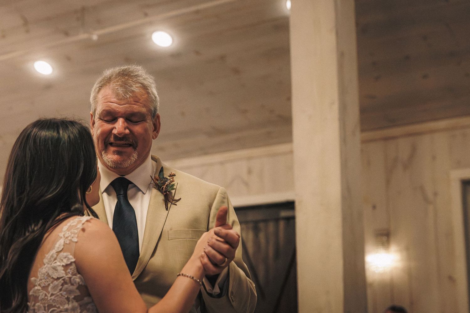 Bride and father sharing emotional first dance at wedding reception in rustic barn venue.