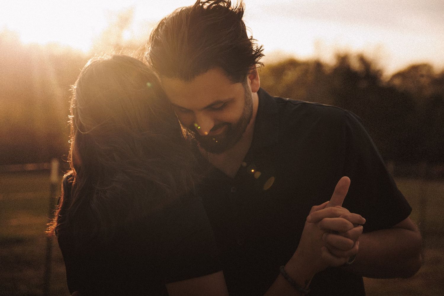 Couple embracing tenderly at golden sunset in a park, warm sunlight glowing behind them.