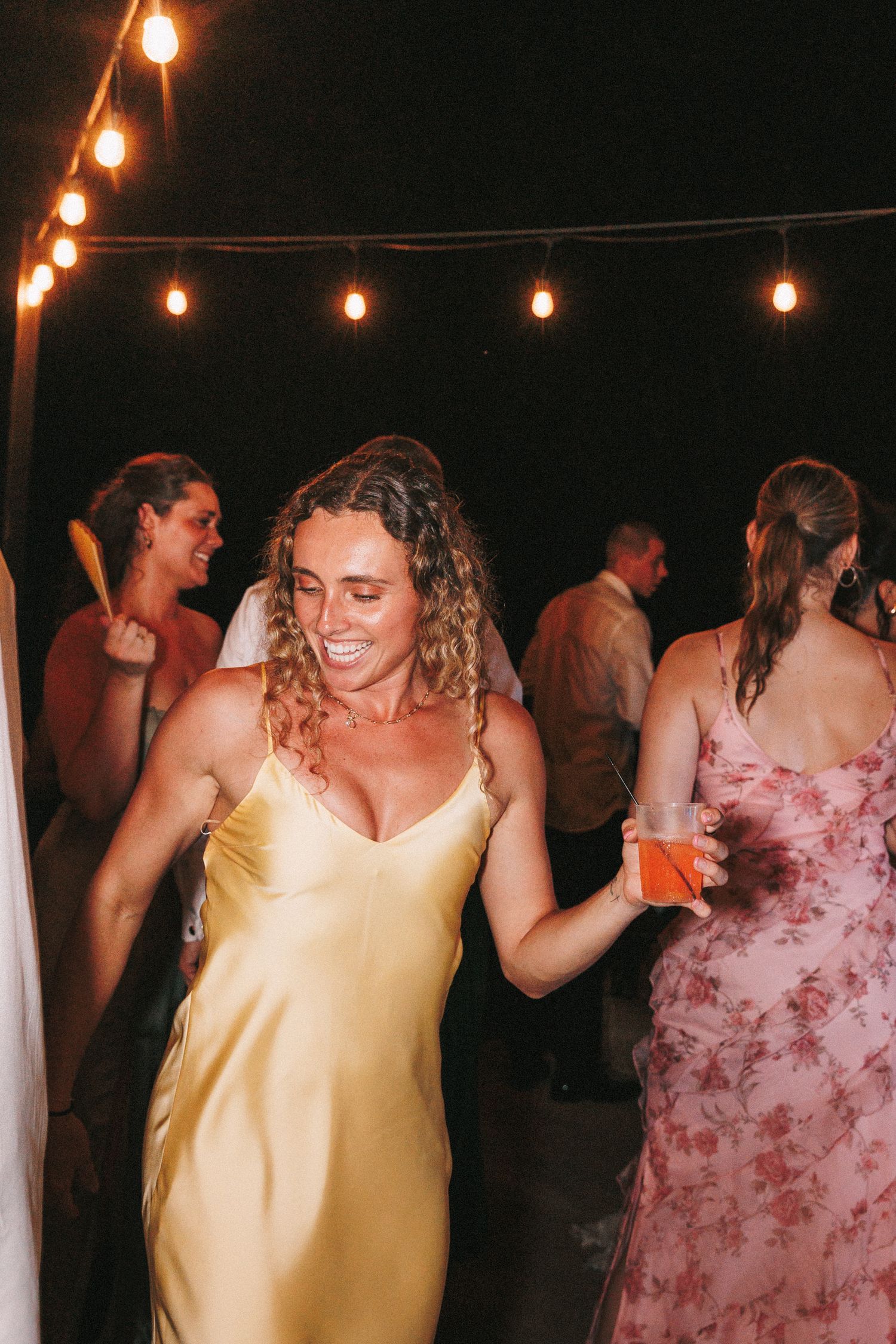 Wedding guests dancing under string lights at an outdoor nighttime reception.