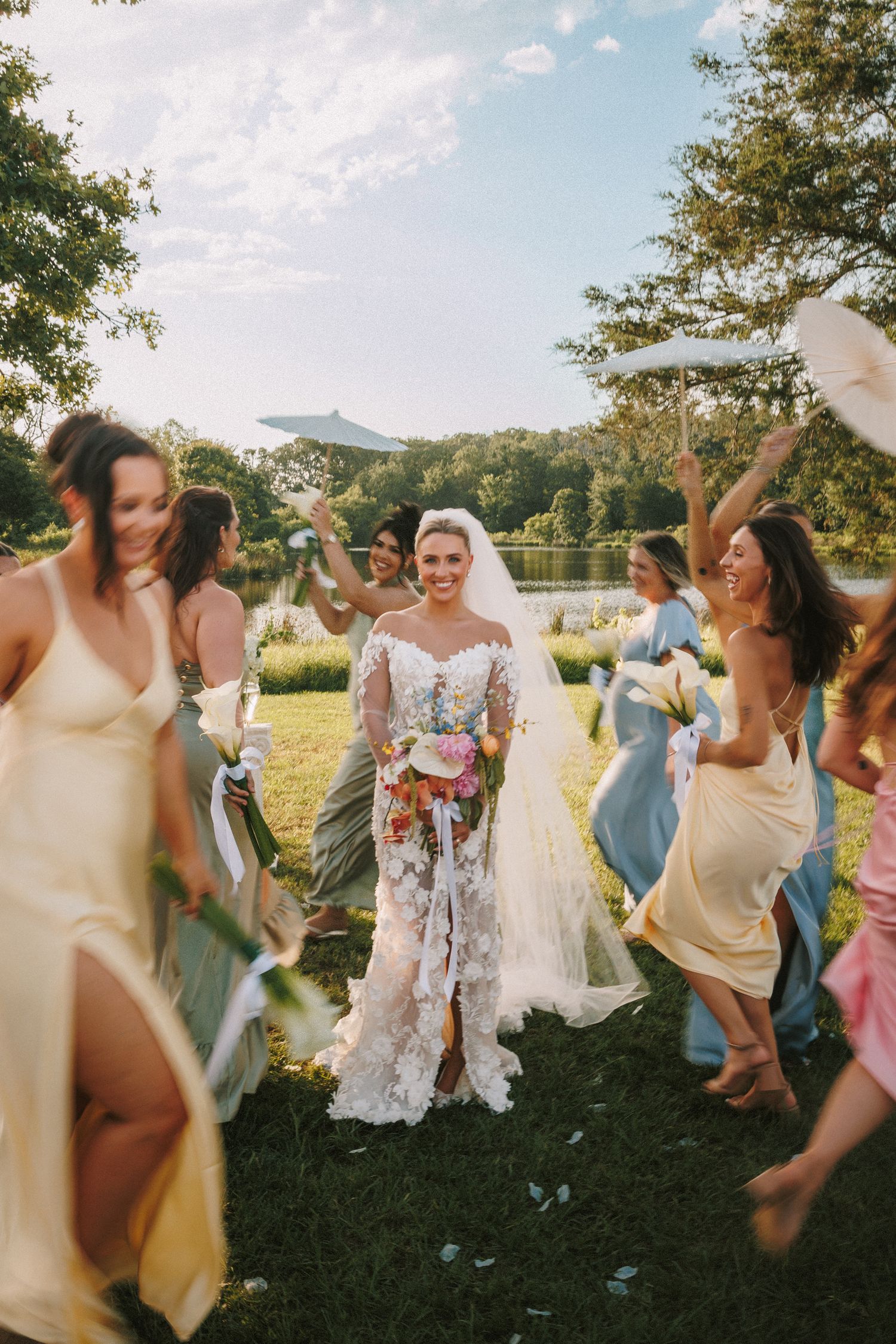 Wedding party dancing joyfully on a grassy lawn with mountains visible in the background.