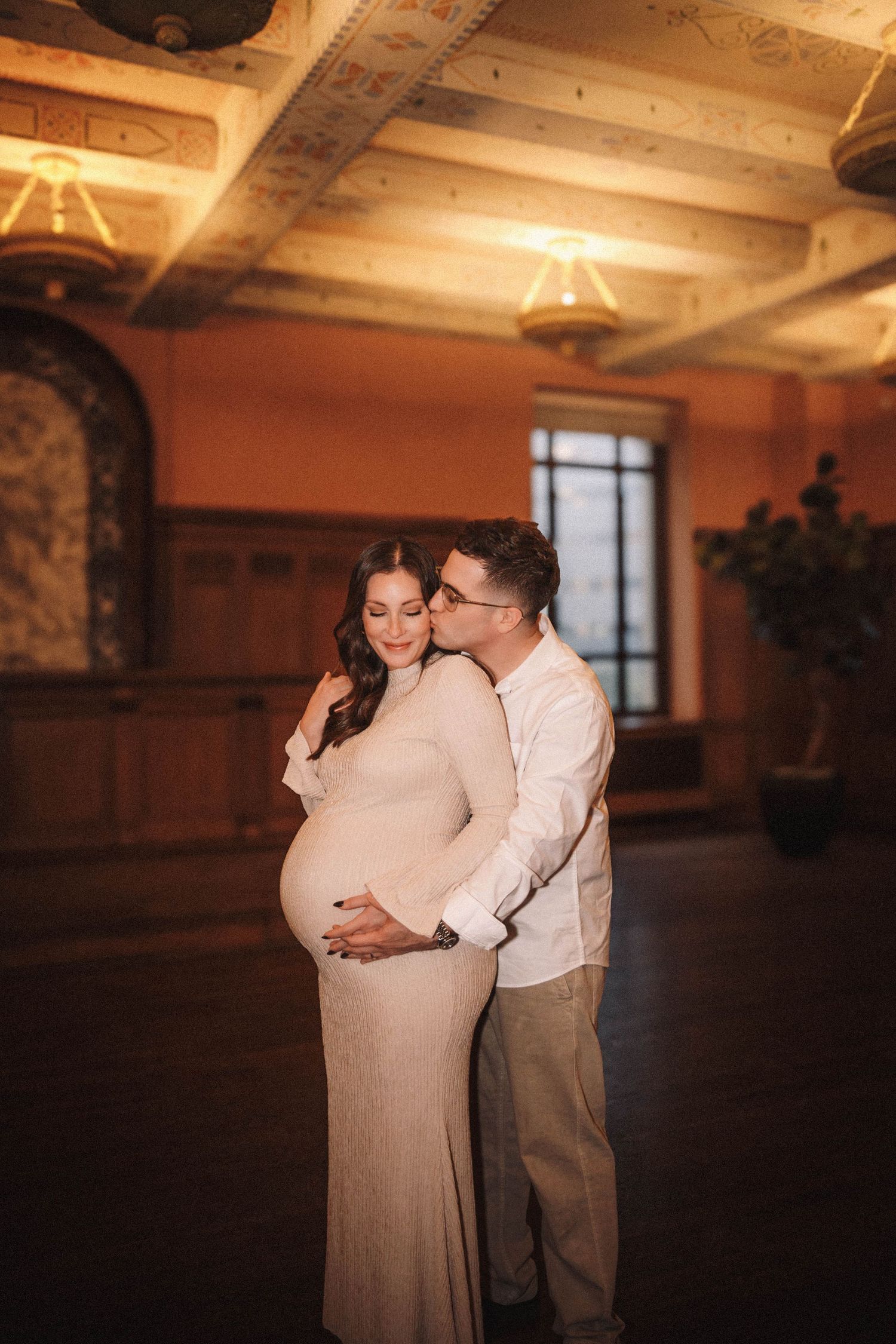 A romantic couple shares a tender moment in a dimly lit venue with ornate architecture.