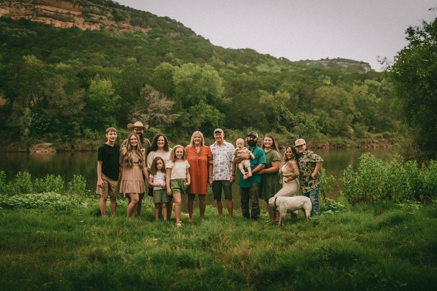 Group of people gathered outdoors in a grassy meadow with green hills in the background at sunset.