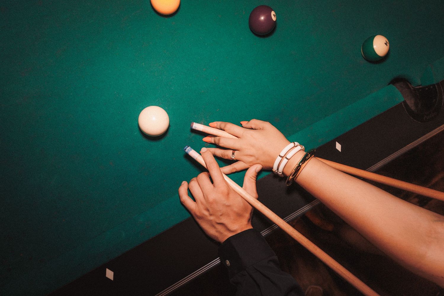 Close-up of billiard balls and pool cues on a green felt table during an intense game of pool.