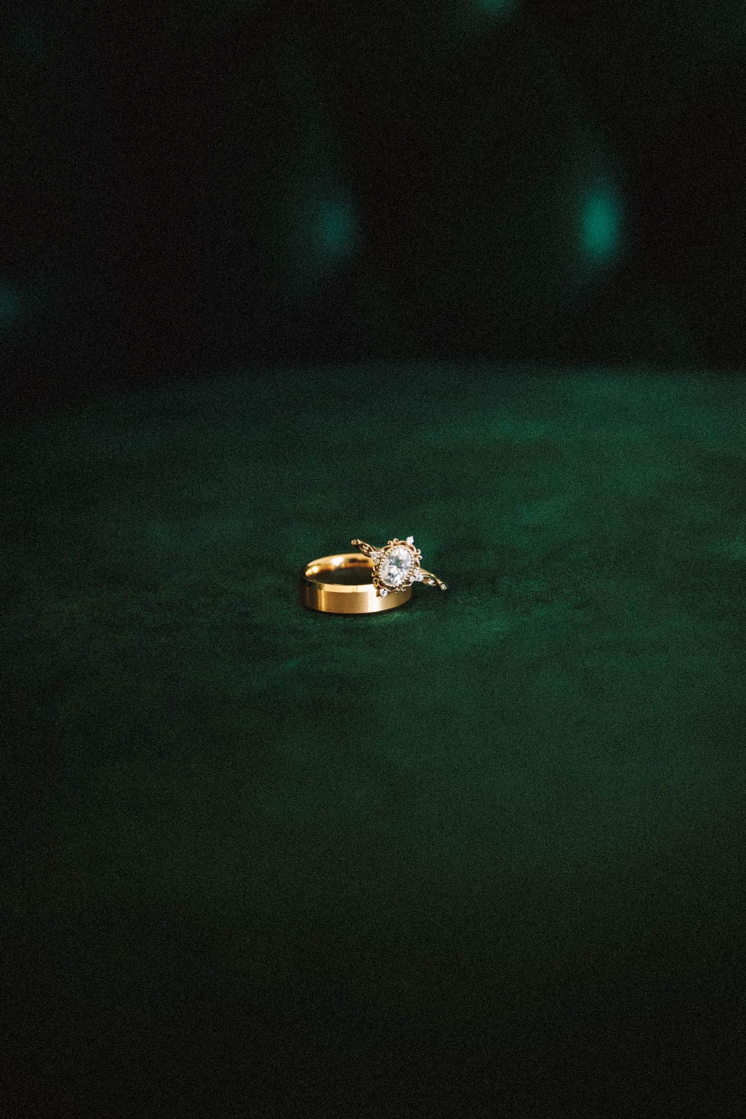 A gold engagement ring with a diamond solitaire sits elegantly against a dark green background.