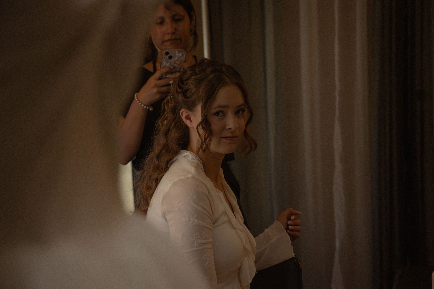 Bride smiling as bridesmaid styles her elegant updo hairstyle before the wedding ceremony.