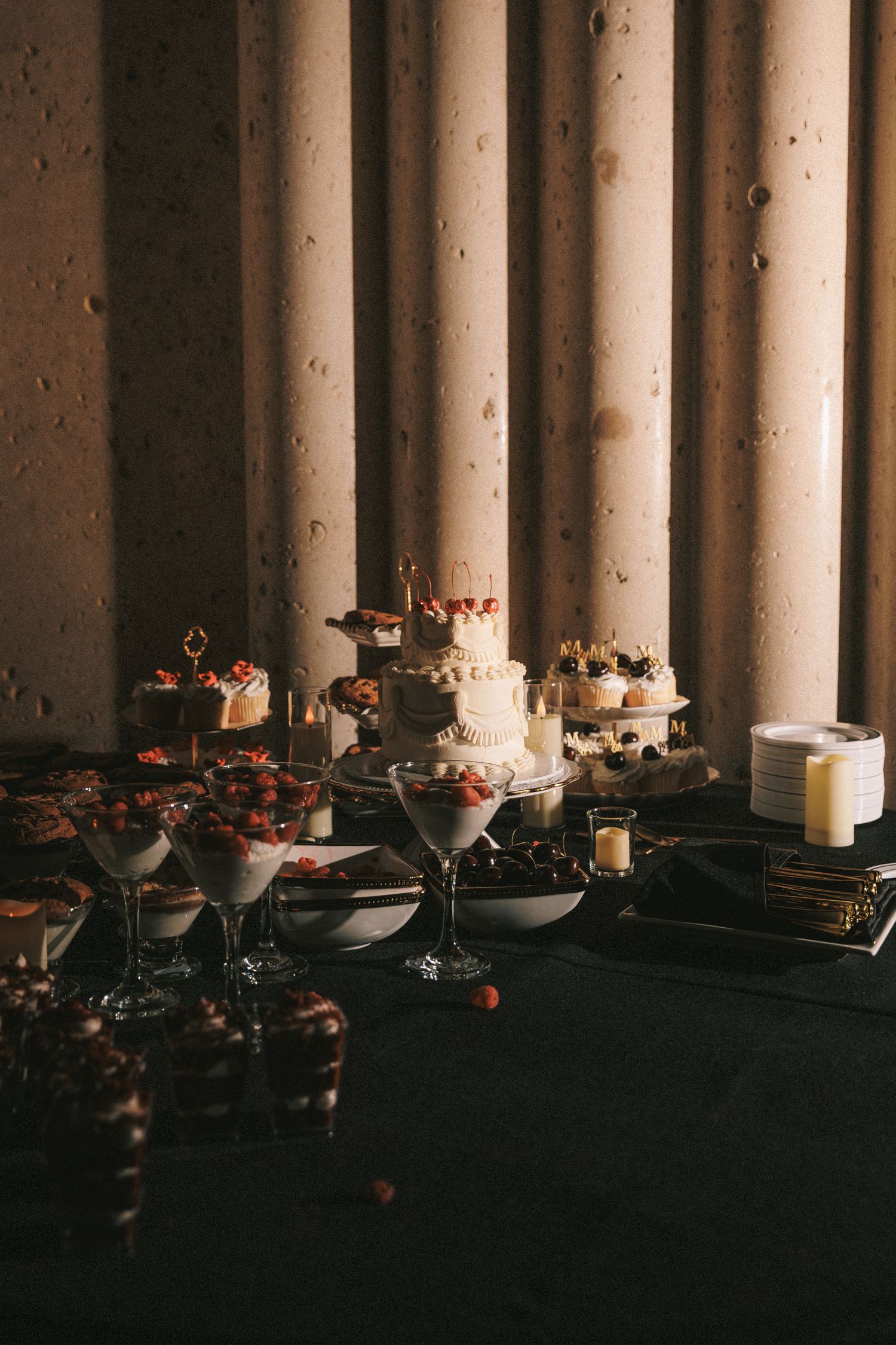 Elegant wedding dessert table with tiered cake, cupcakes and strawberry parfaits by stone columns.