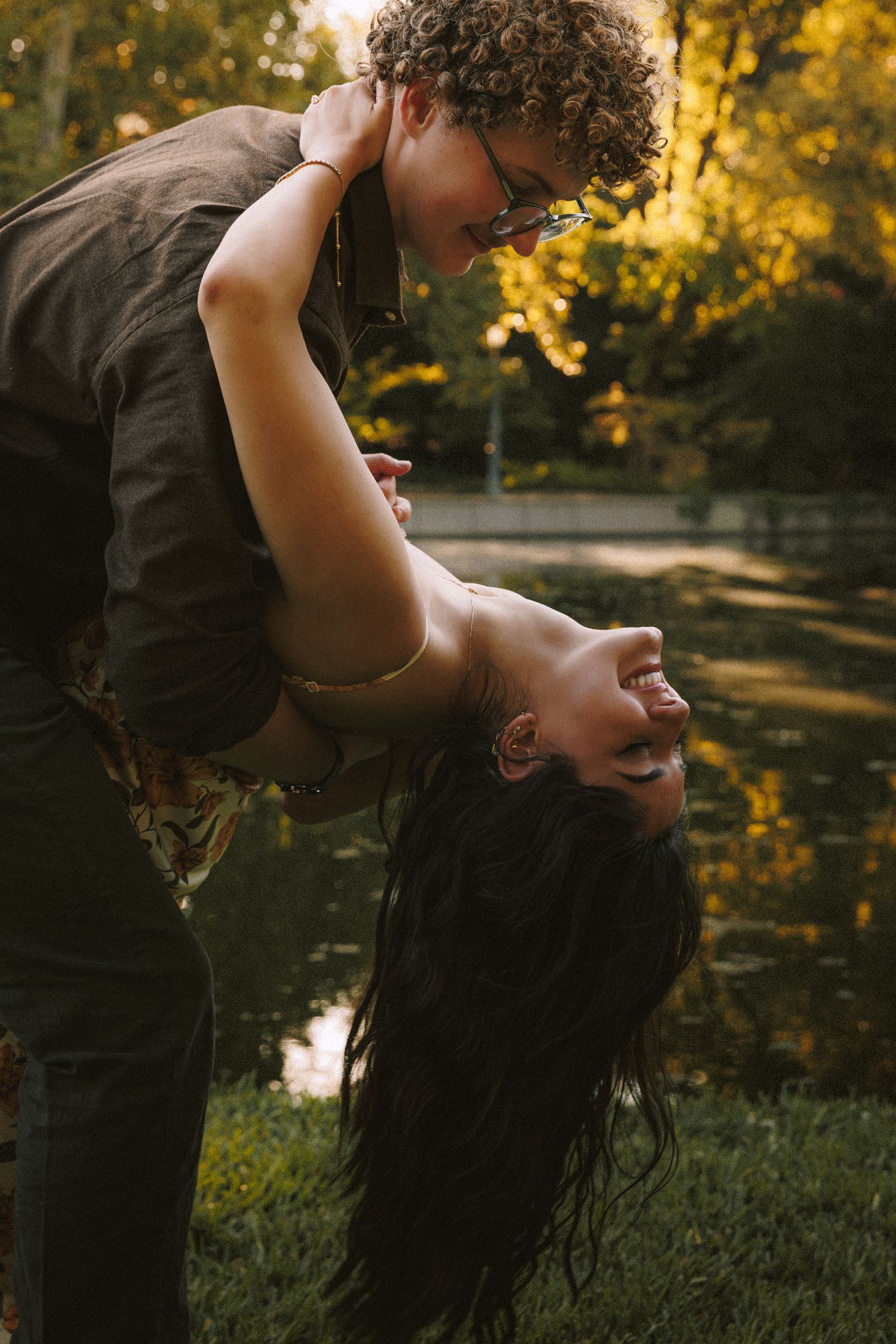 A couple dances together in a romantic embrace against a golden sunset in a park setting.