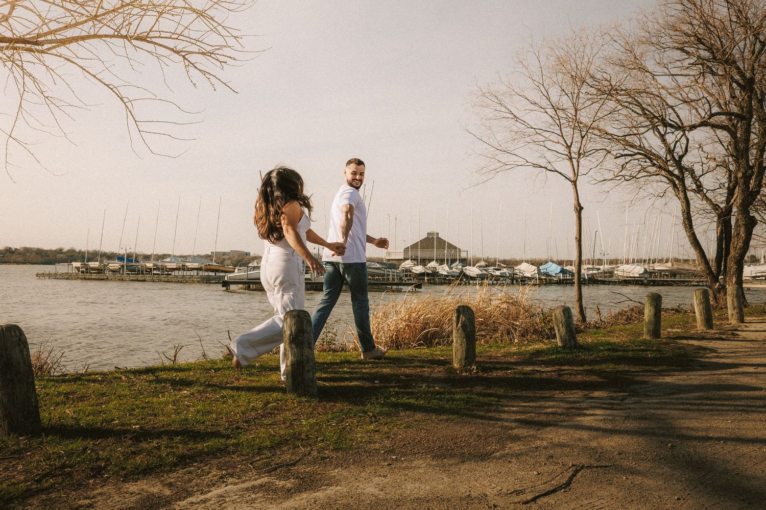 Silhouetted couple walks hand in hand along a waterfront path during sunset.