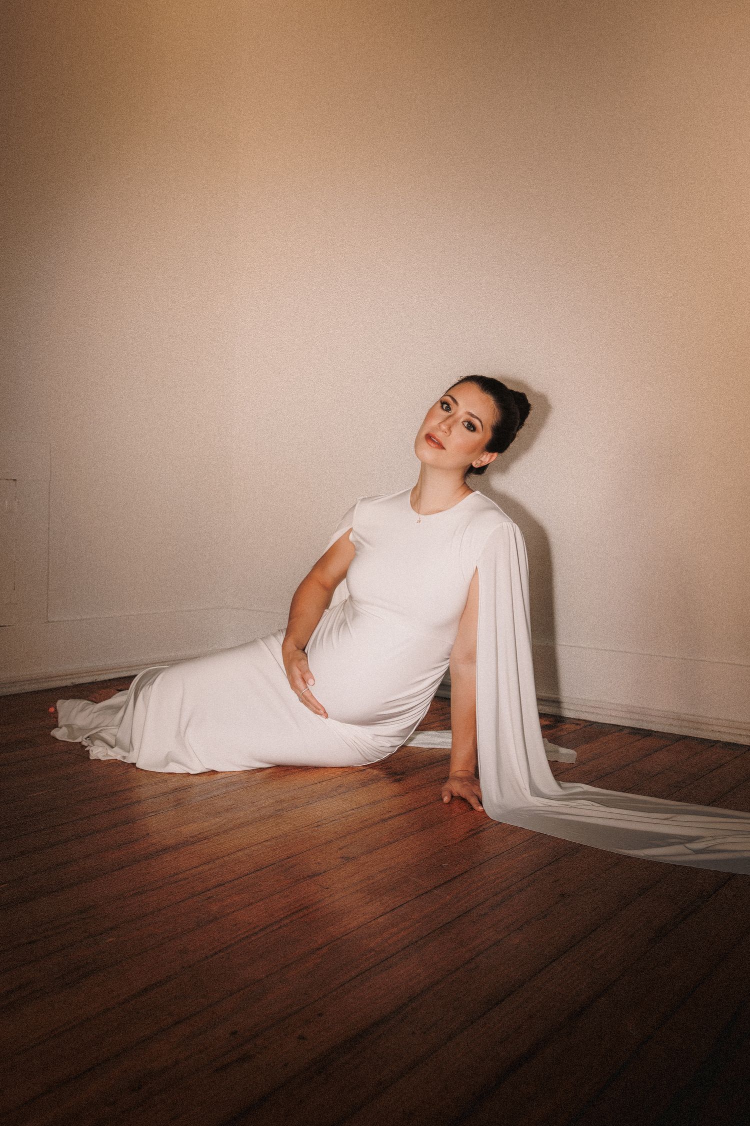 A figure in white clothing performs a dramatic dance sequence across a dark wooden floor against a beige wall.