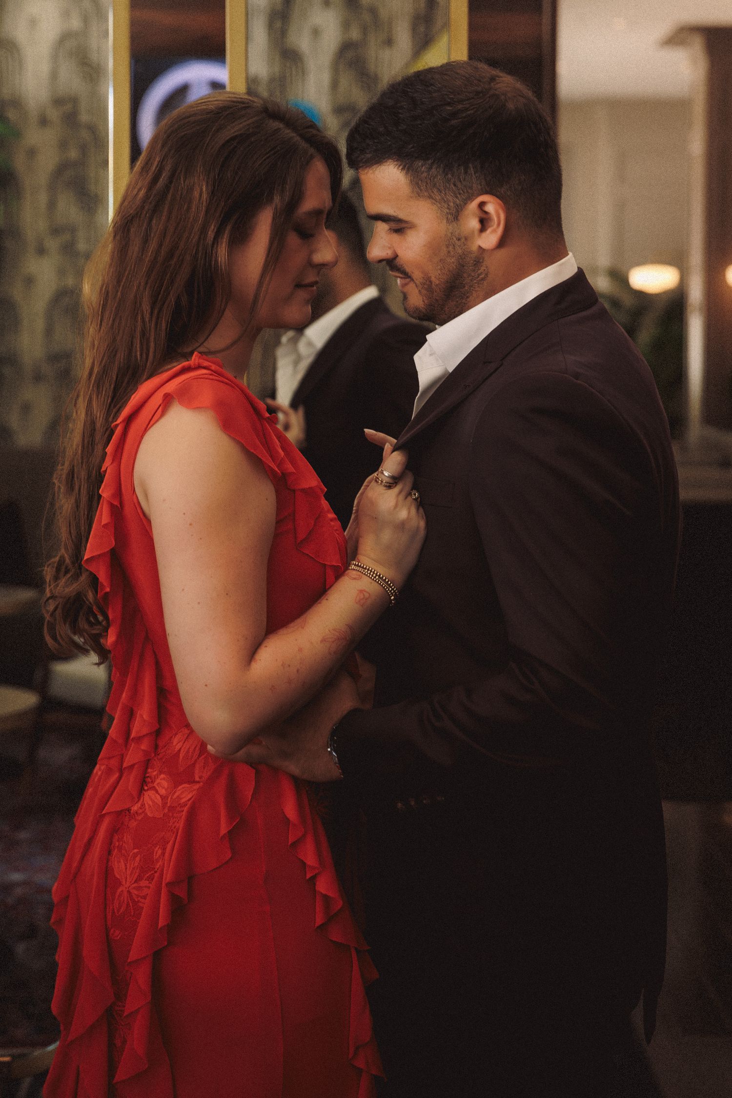 Couple in elegant attire sharing a romantic moment, woman in red ruffled dress, man in dark suit.