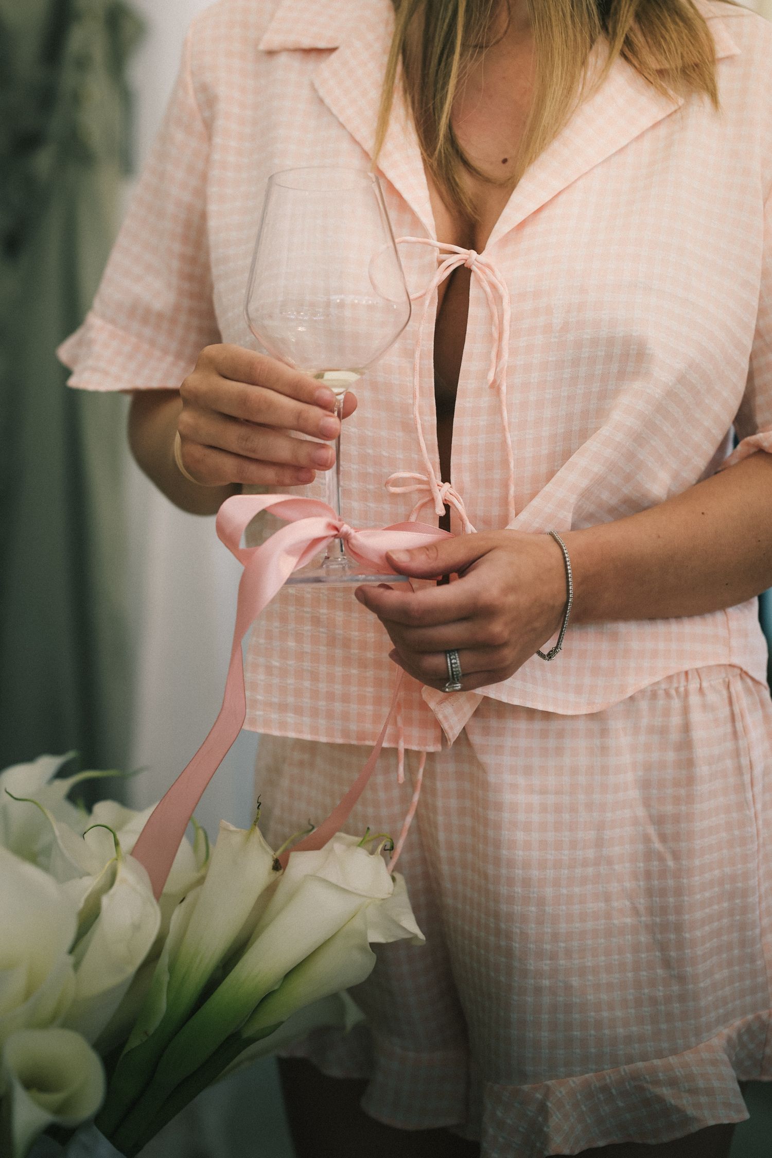 Pink gingham dress is shown in detail with white calla lilies in the foreground during wedding preparations.