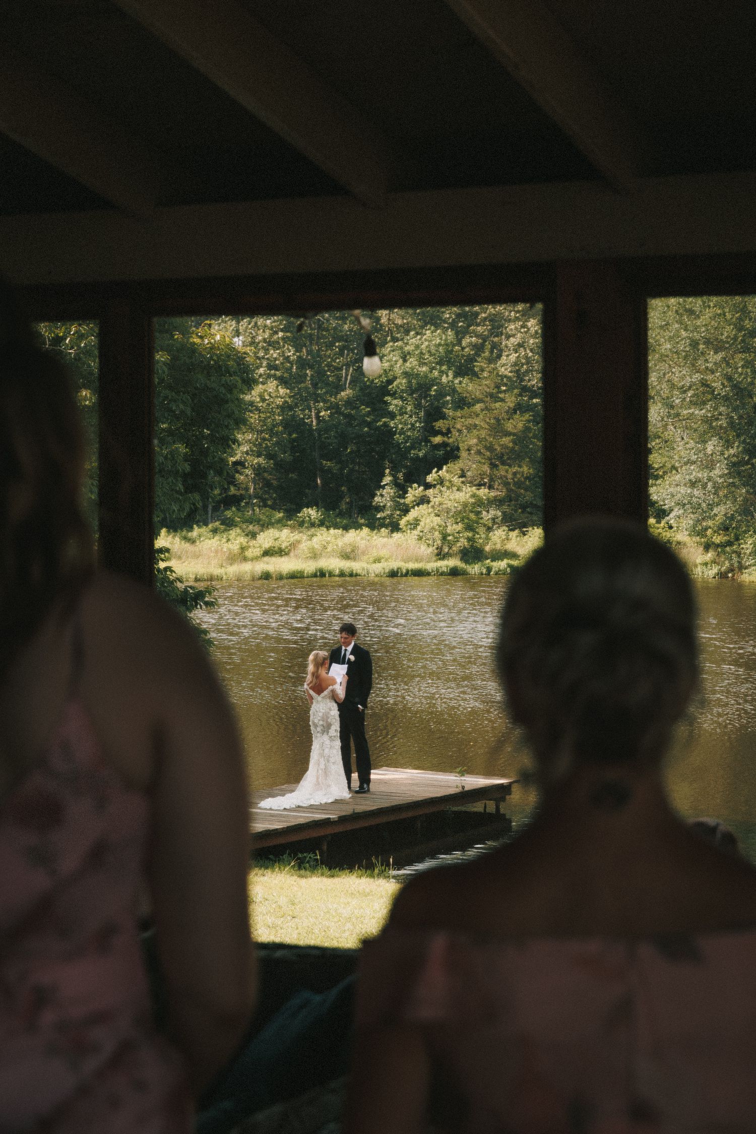 A wedding couple poses for romantic photos on a wooden dock by a serene lake during golden hour.