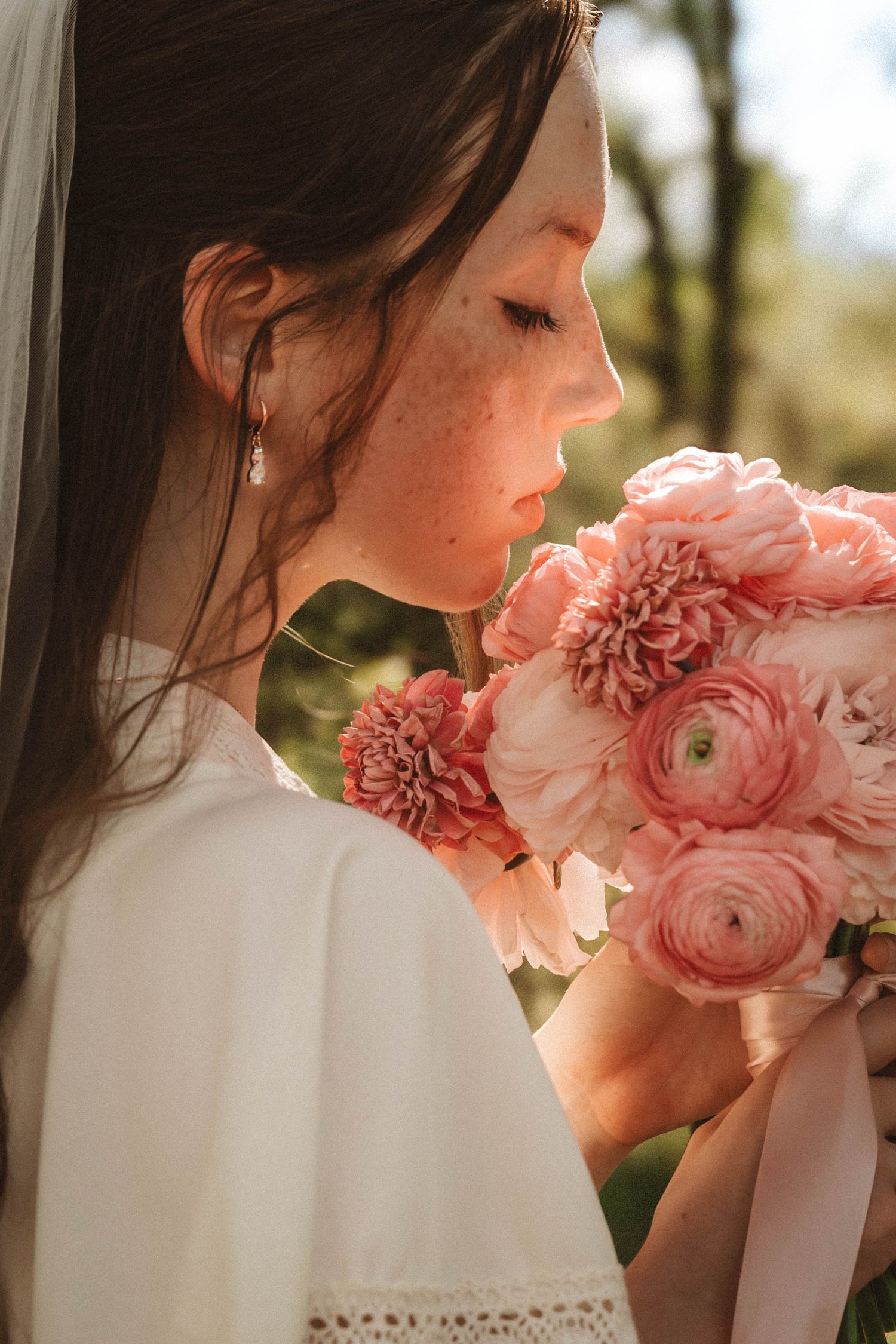 A close-up profile view holding a romantic bouquet of pink ranunculus and dahlias in warm golden sunlight.
