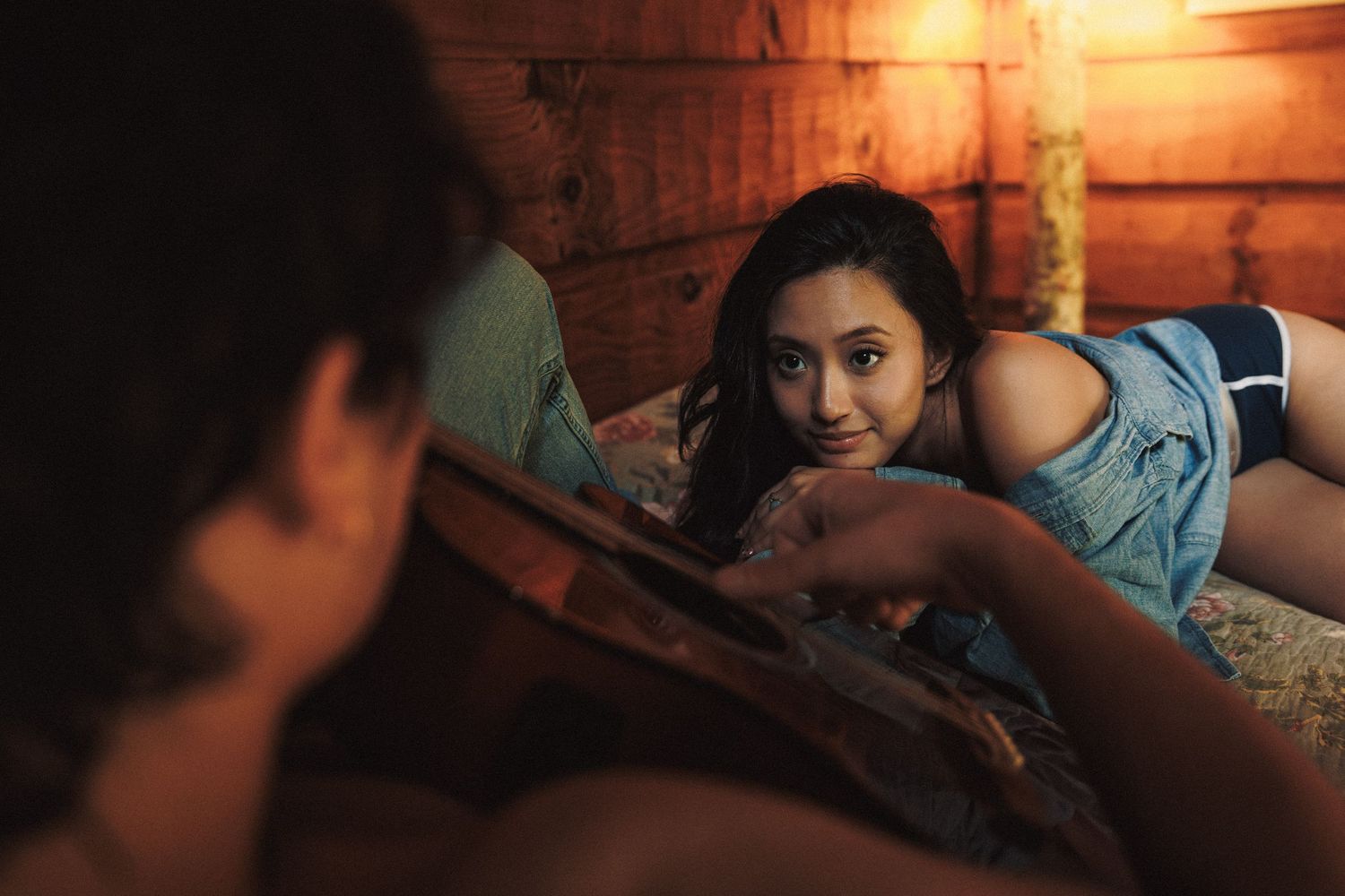 A person in a blue tank top lying down in a warm, wood-paneled room with atmospheric lighting.