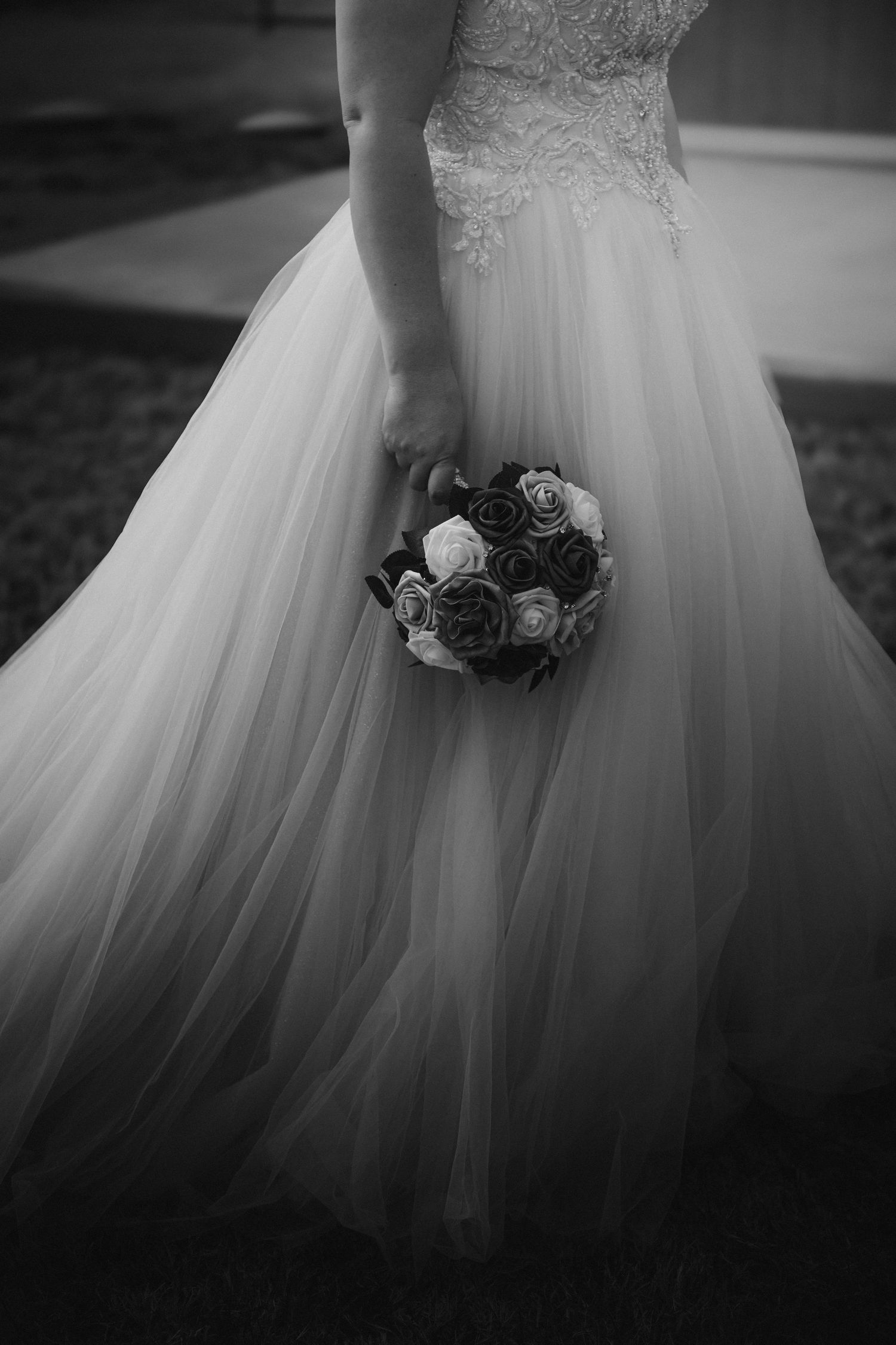 Close-up detail of a white tulle wedding dress and bouquet in black and white photography.