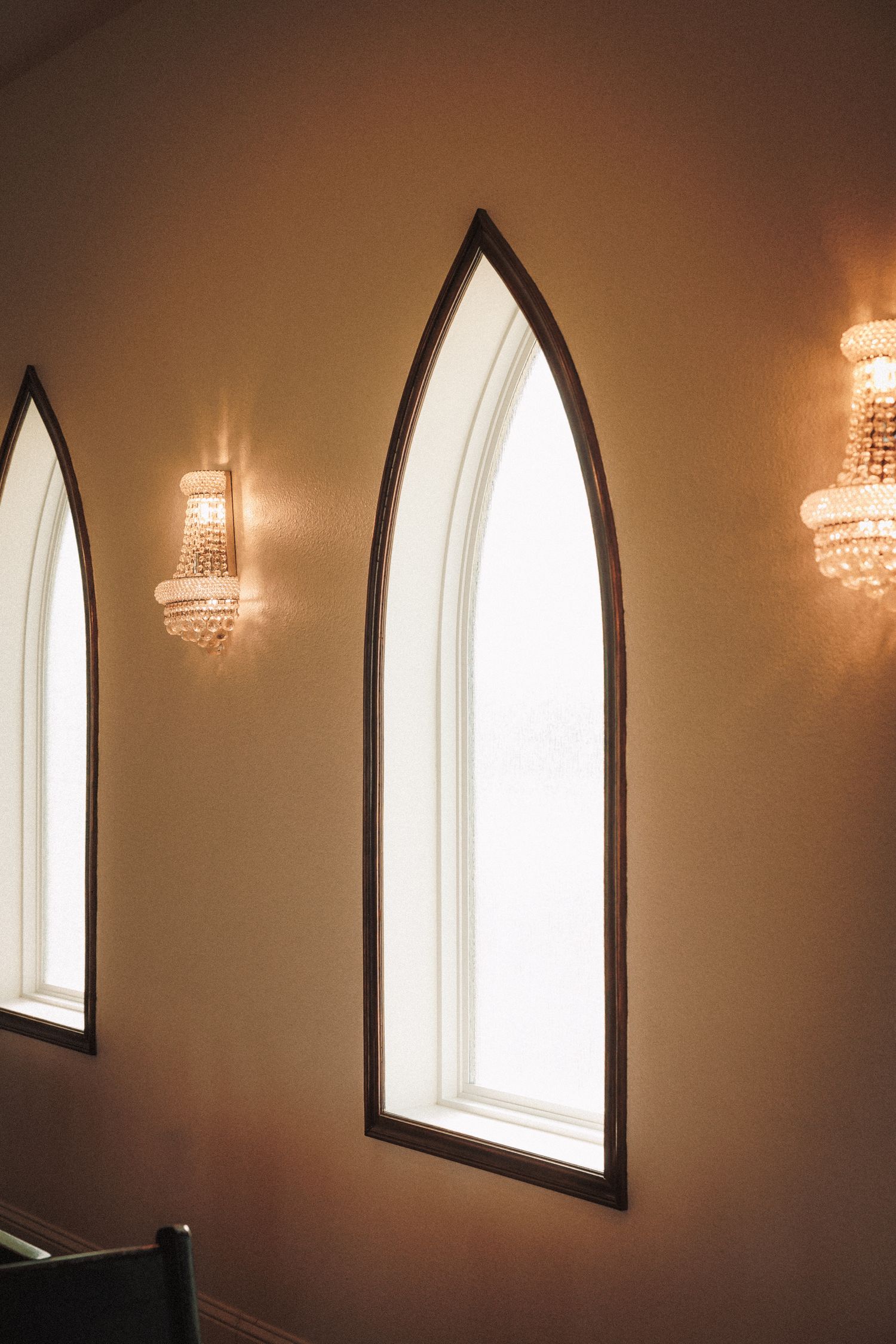 Gothic arch windows with crystal wall sconces in a warmly lit chapel interior.