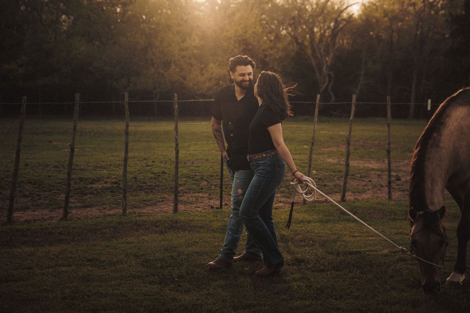 Couple laughing and walking with a horse at golden hour on a rustic farm.