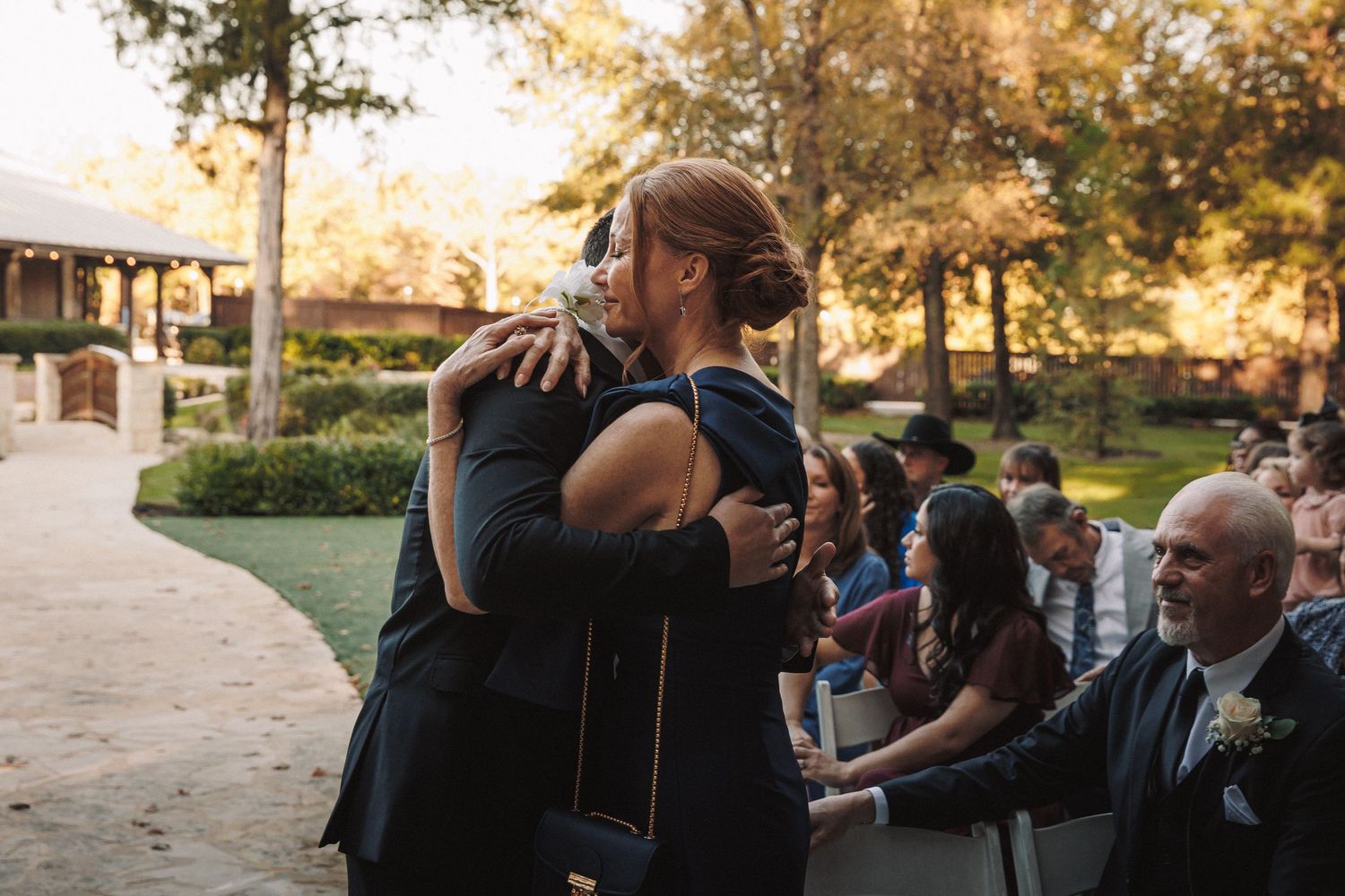 Woman in navy dress sharing an emotional hug with a guest at an outdoor fall wedding ceremony.