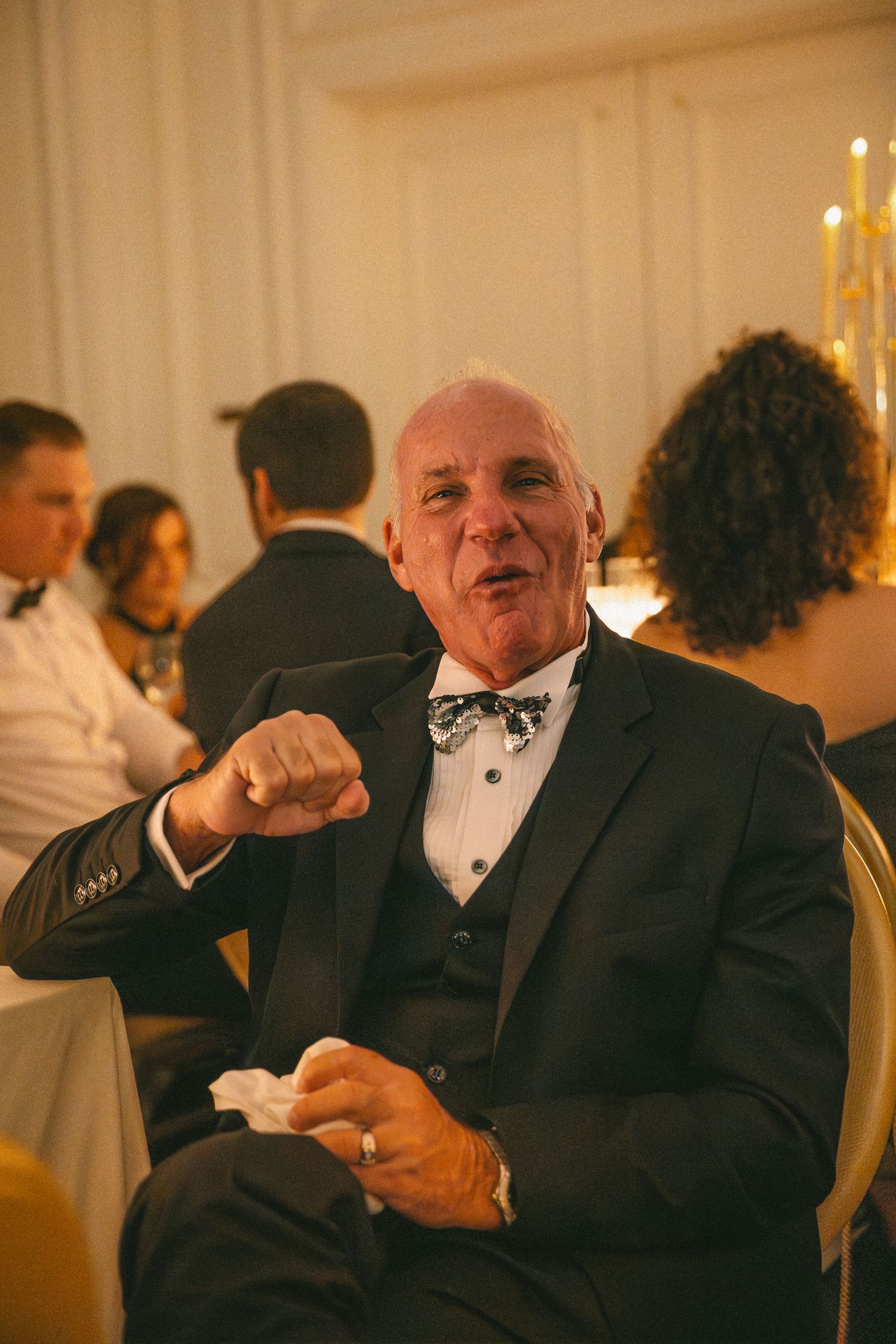 Cheerful older gentleman in black tuxedo with bow tie enjoying a wedding reception dinner.
