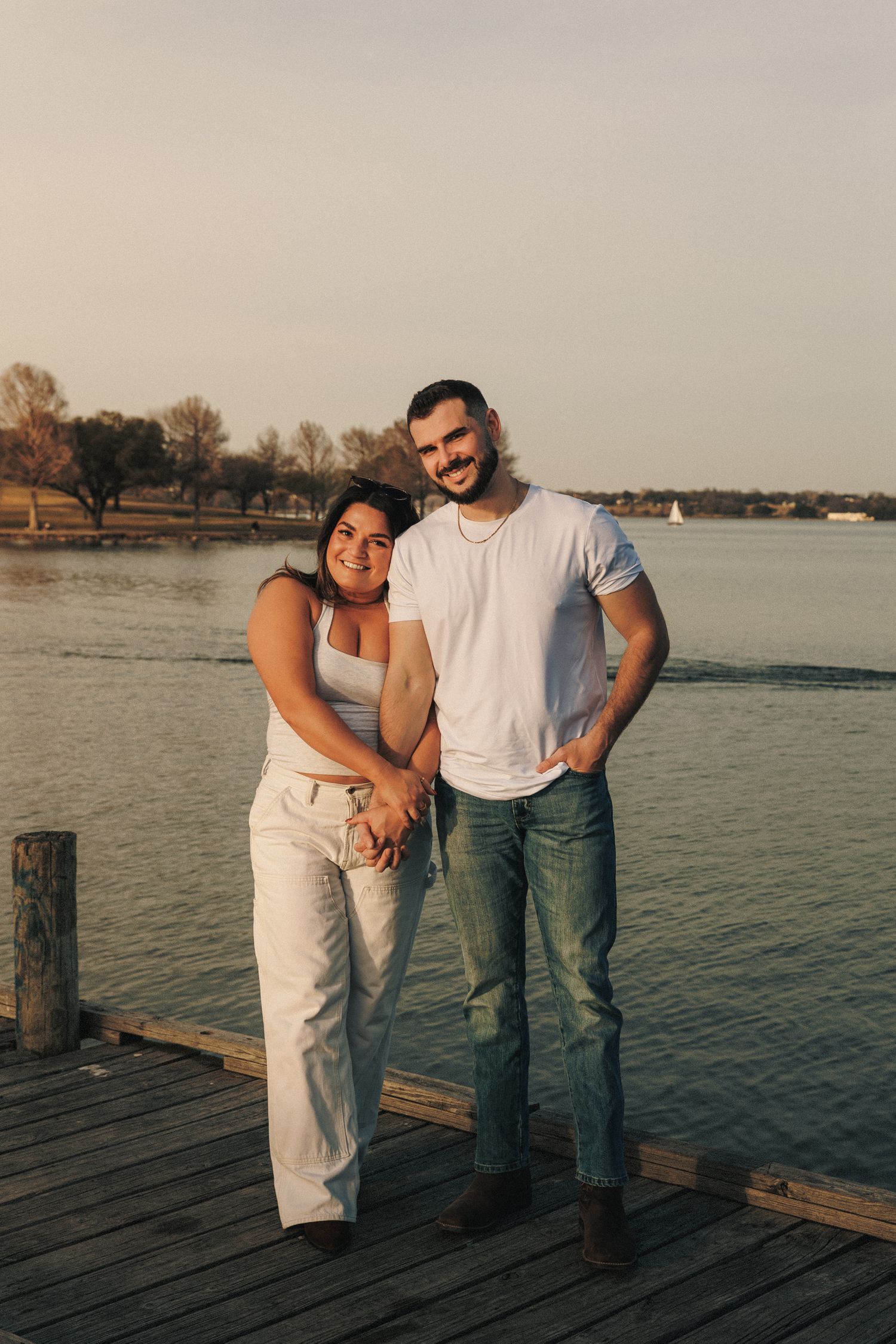 Couple standing together on wooden pier overlooking lake at golden hour.