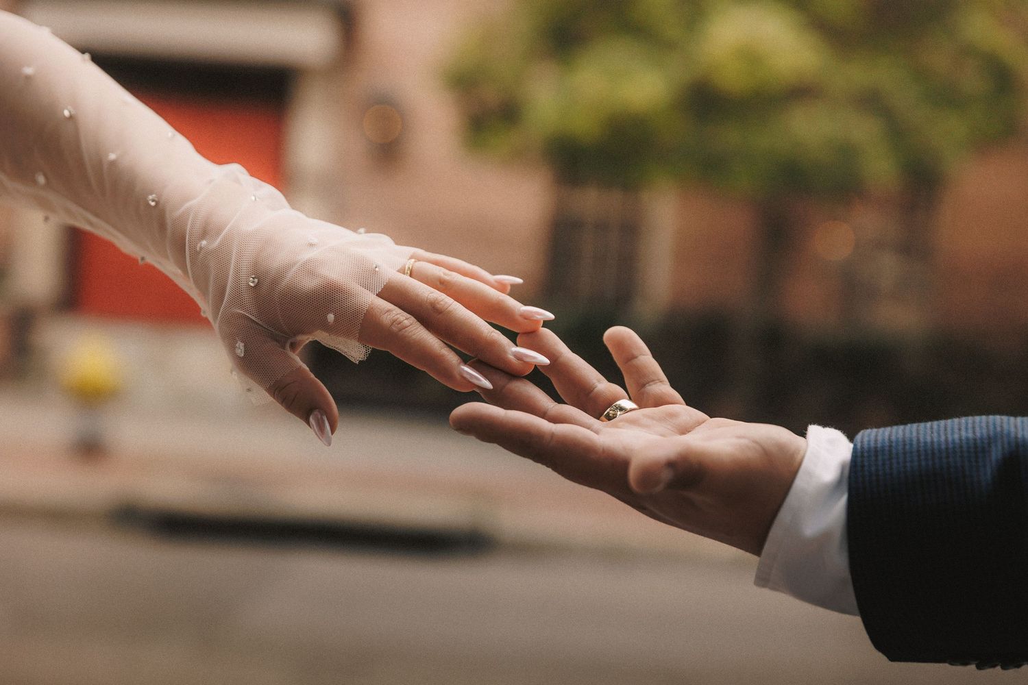 Close-up of hands reaching toward each other against a blurred outdoor background.