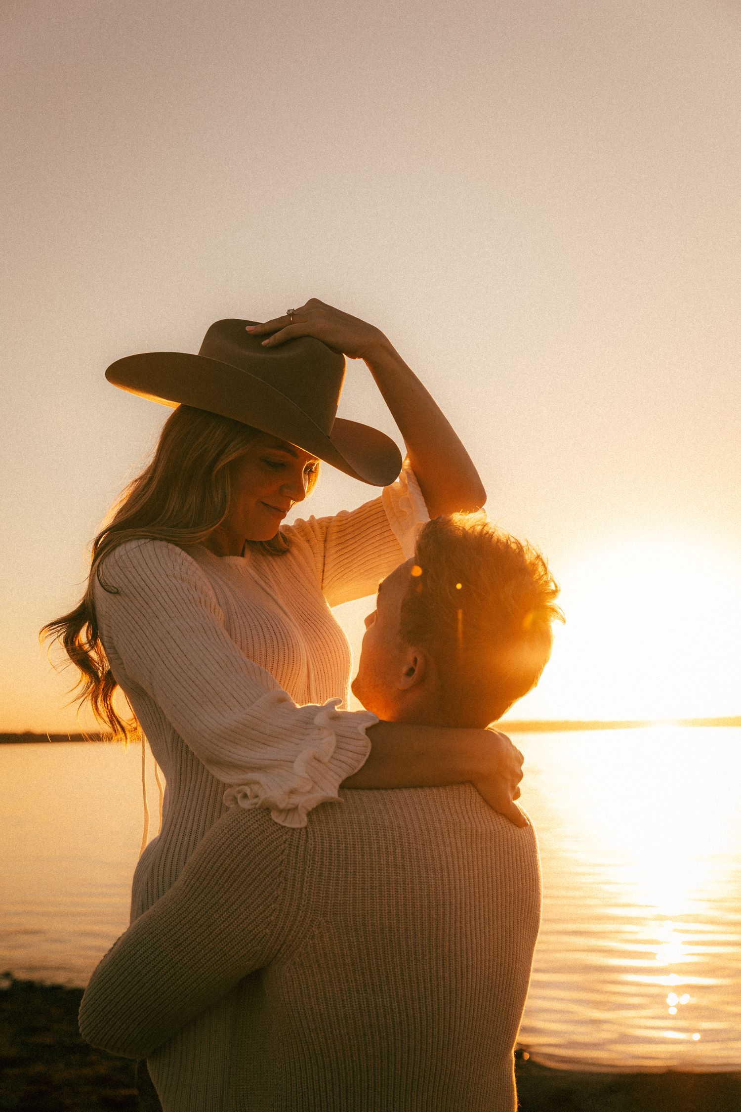 Intimate couple sharing tender moments on beach at sunset with water reflecting golden light.