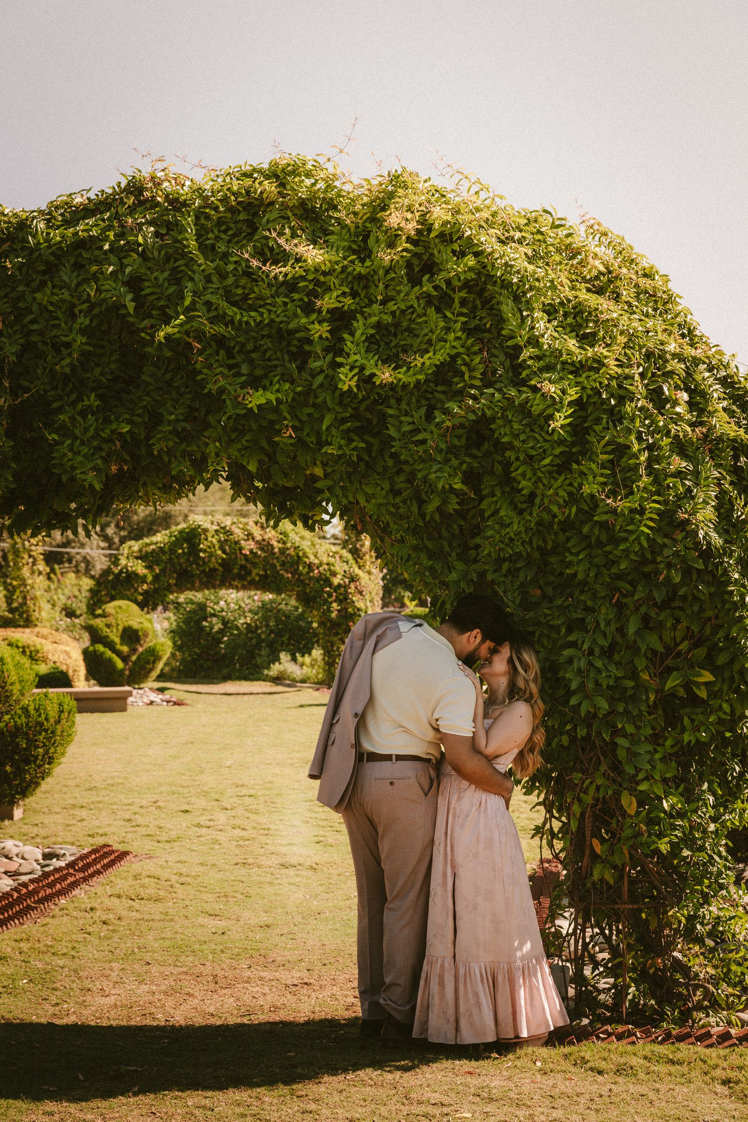 A romantic moment under a natural green archway in a garden setting.