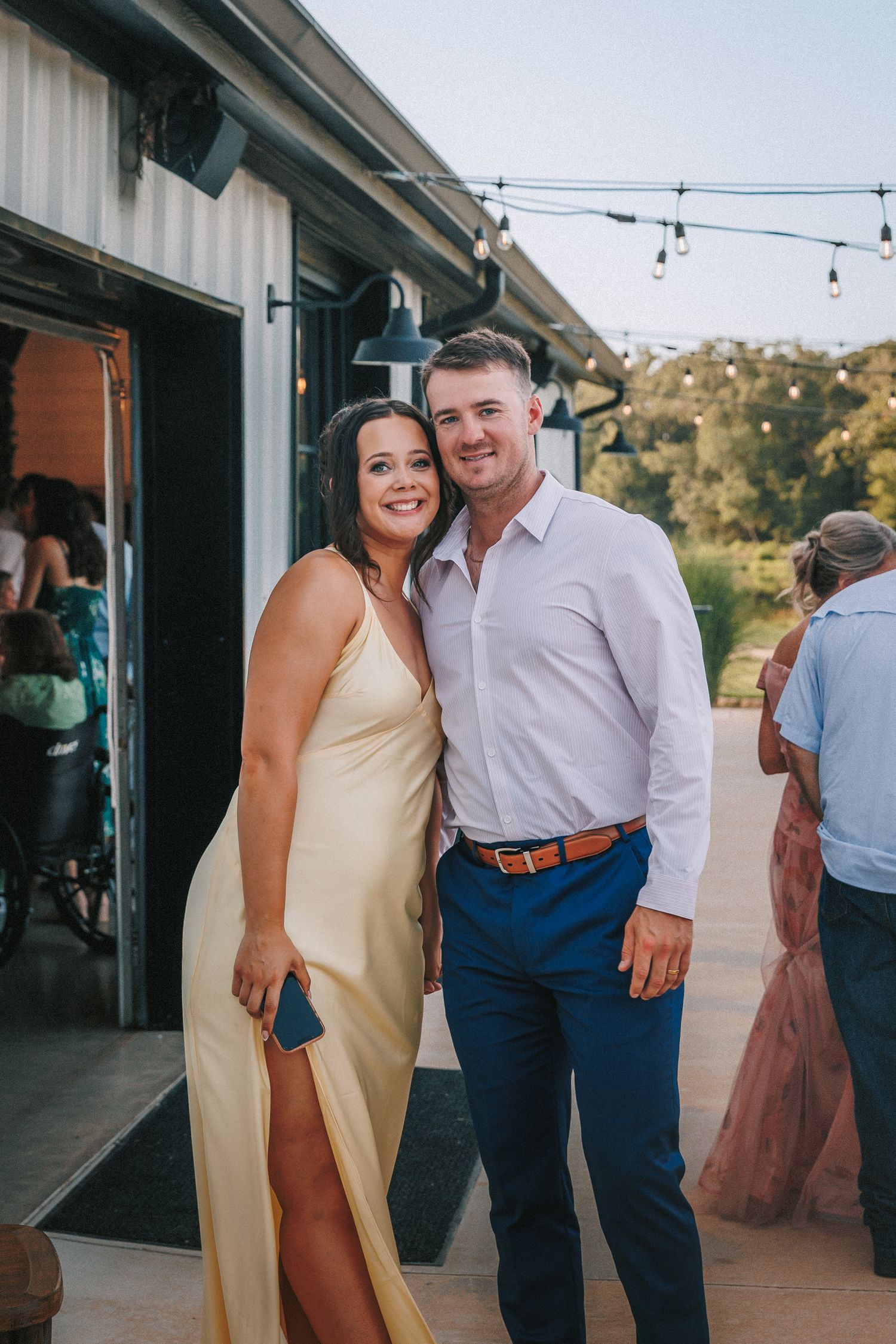 Wedding guests enjoying a reception party on an outdoor venue patio with string lights.