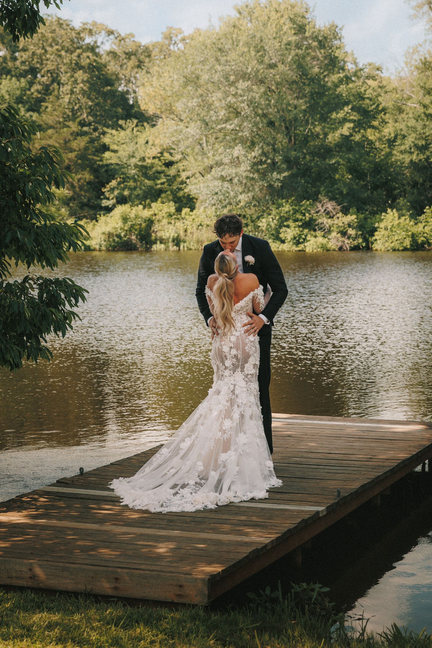 Romantic wedding couple shares intimate dance on wooden dock by serene lake during golden hour.
