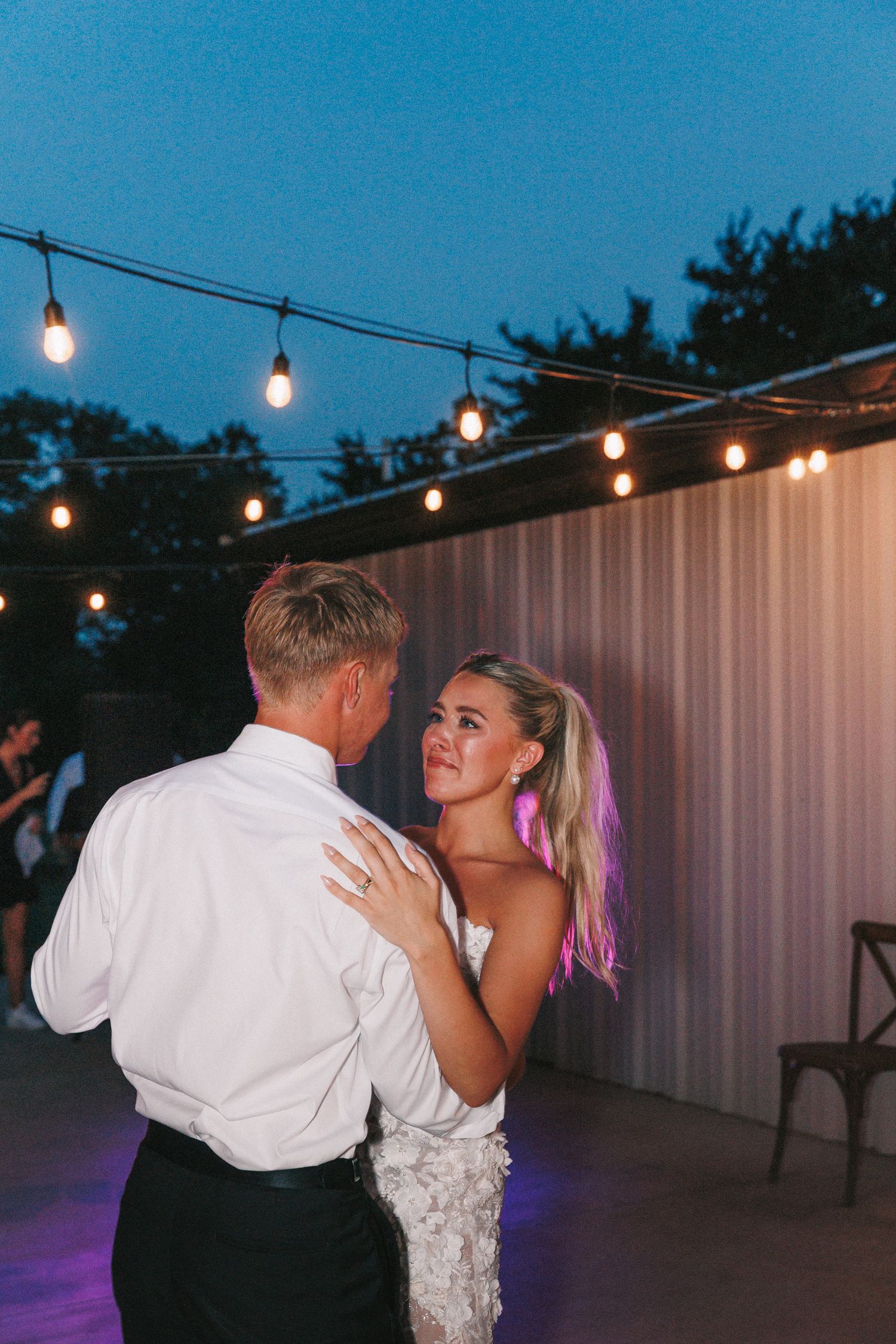 Wedding reception dance floor lit with string lights and a white backdrop.