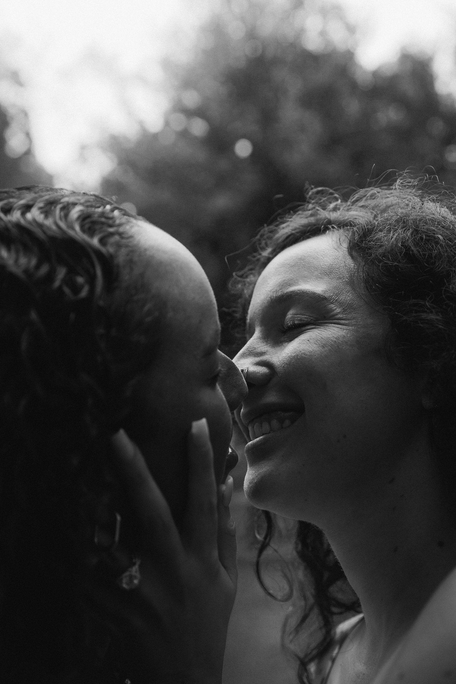 Black and white close up photograph of two people sharing an intimate moment together, captured in dramatic lighting.