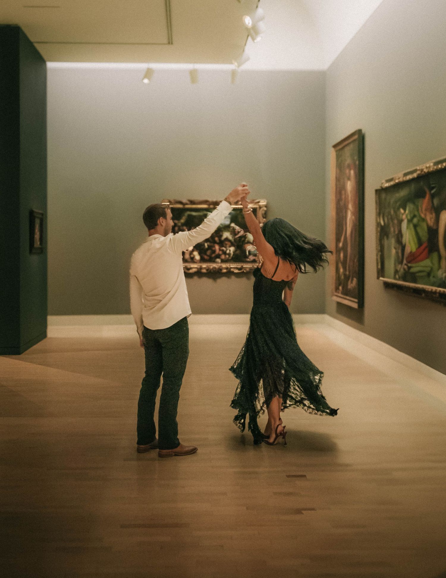 Several people observe and interact with artwork in a minimalist gallery space with wooden floors and white walls.