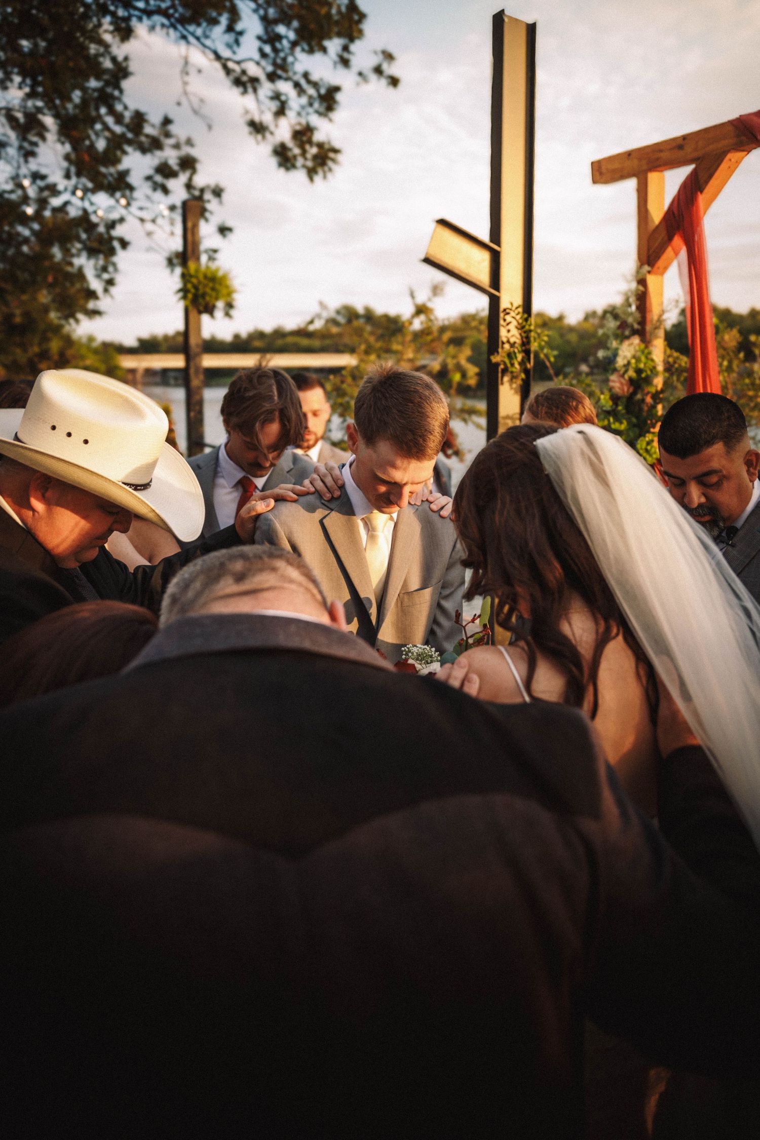 A crowd gathers under wooden beams at an outdoor ceremony during golden hour.