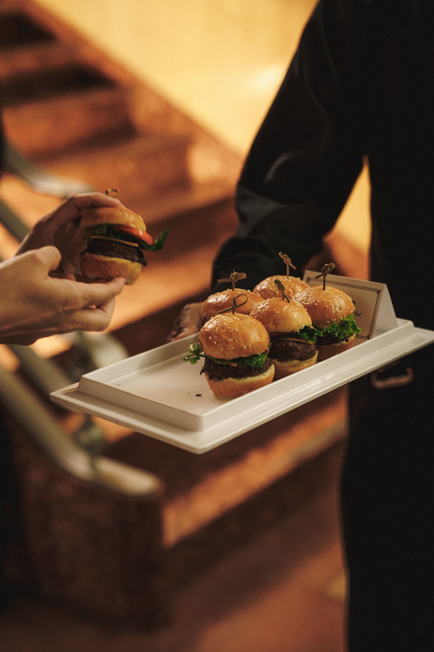 Wedding server presenting a tray of gourmet mini sliders to a guest at an elegant wedding reception.