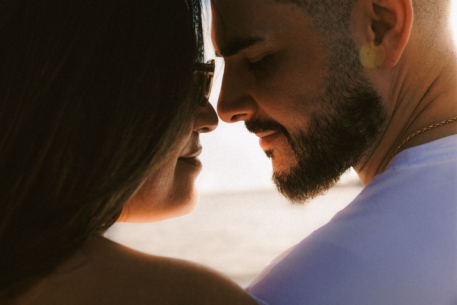 Close up profile silhouette of couple touching foreheads against sunset light.