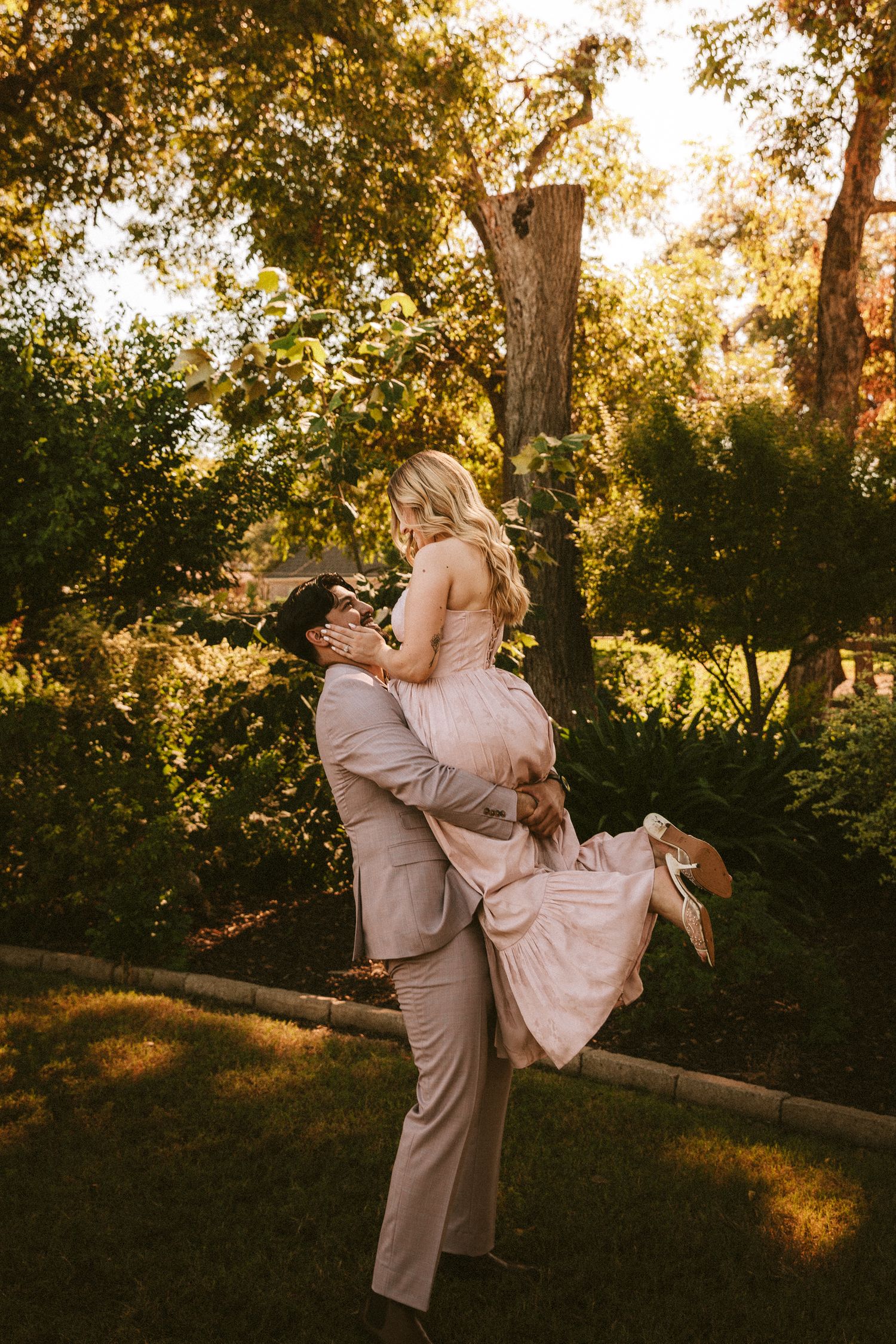 A couple shares a playful lifting moment in a garden during golden hour.