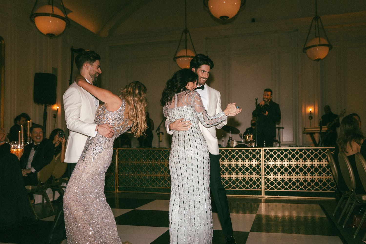 Wedding guests dance together on checkered floor at elegant evening reception celebration.