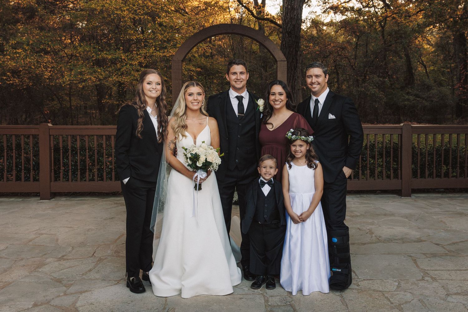 Wedding party family portrait with bride and groom surrounded by relatives in autumn outdoor setting.